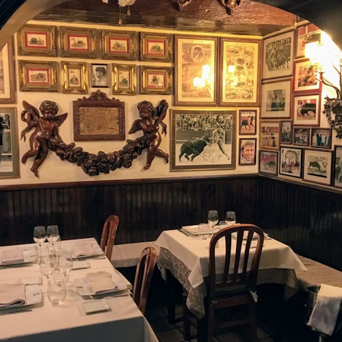 פינת מסעדה נעימה עם תמונות ויצירות אמנות ממוסגרות על הקירות, מקושטת בפסלי מלאכים מעל שני שולחנות מוכנים.