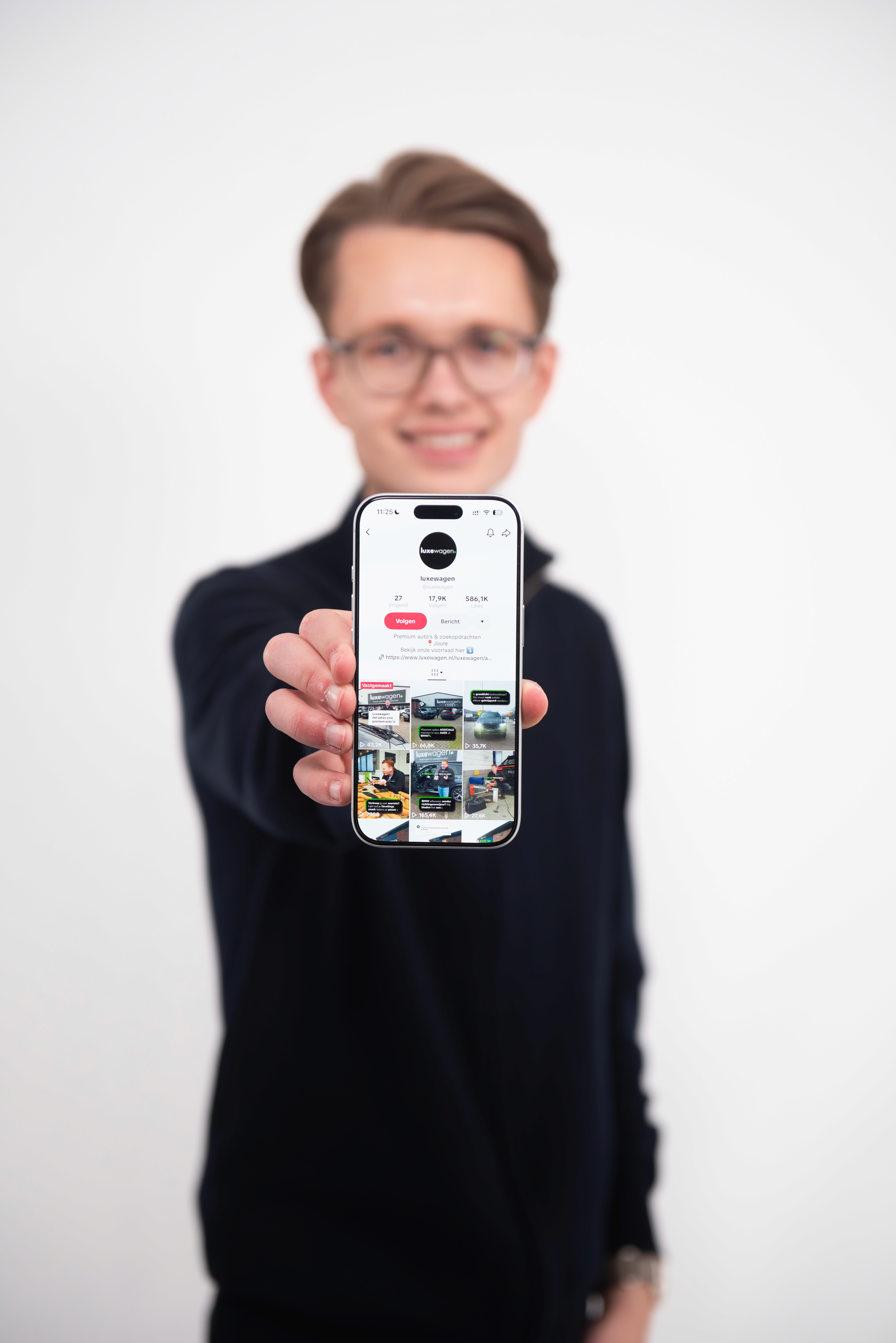 A person with curly hair and glasses smiles at the camera, seated in a cozy workspace with warm lighting.