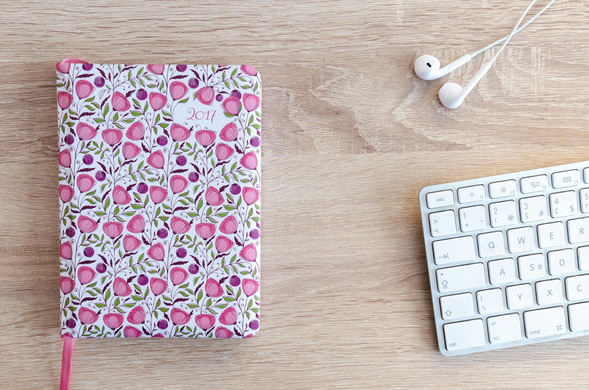 A vibrant floral planner from 2017 on a wooden desk with a keyboard and earphones.
