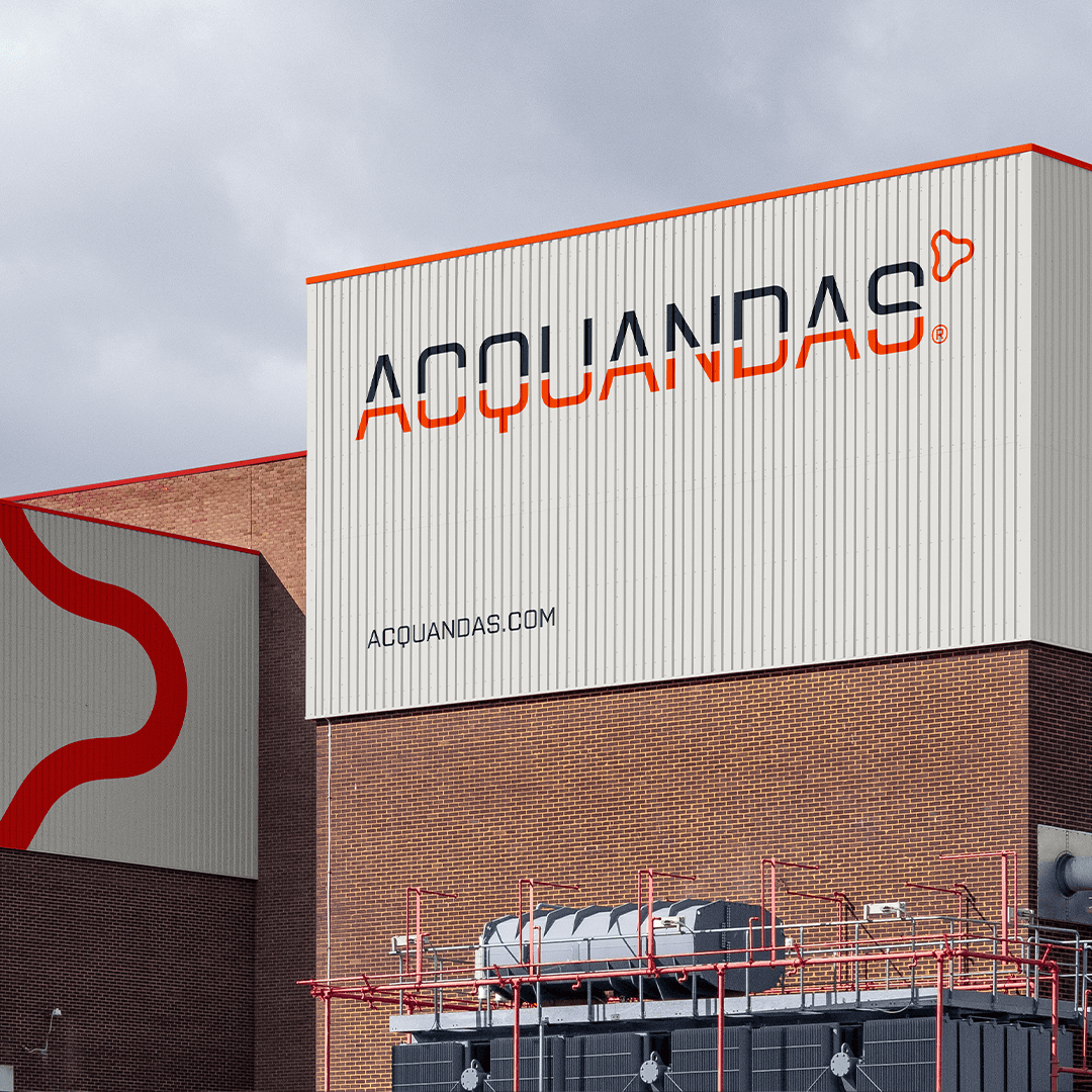 Exterior view of a modern industrial building with the ACQUANDAS logo on the metal facade.