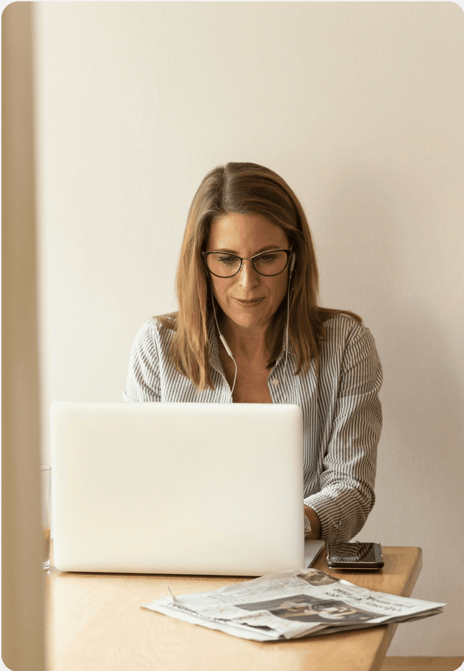 Woman sitting at a table using a computer, news paper on the table.