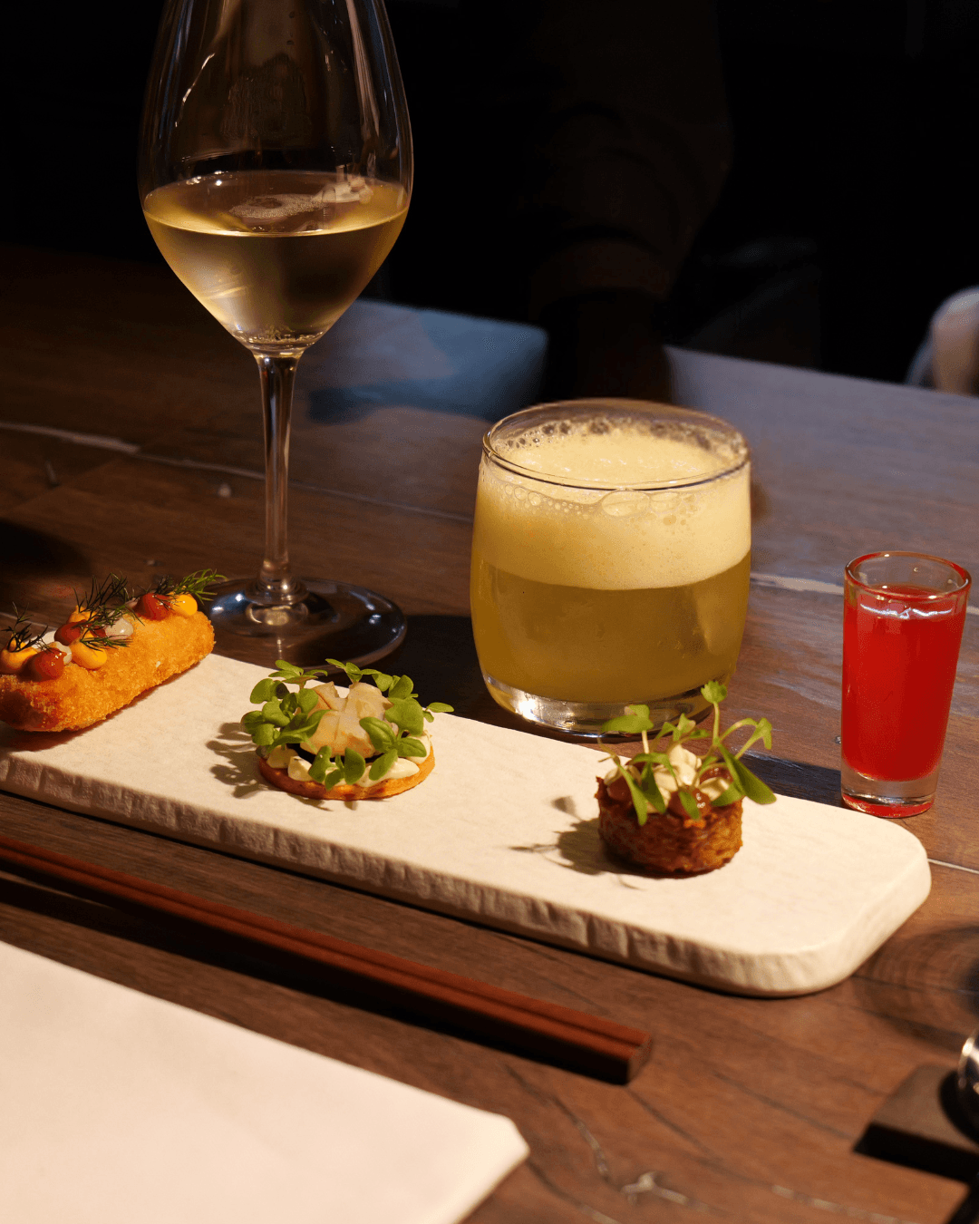 Plate with a seared salmon fillet topped with green herb garnish and sauce, served on a white dish placed on a dark green marble table beside a white candlestick.