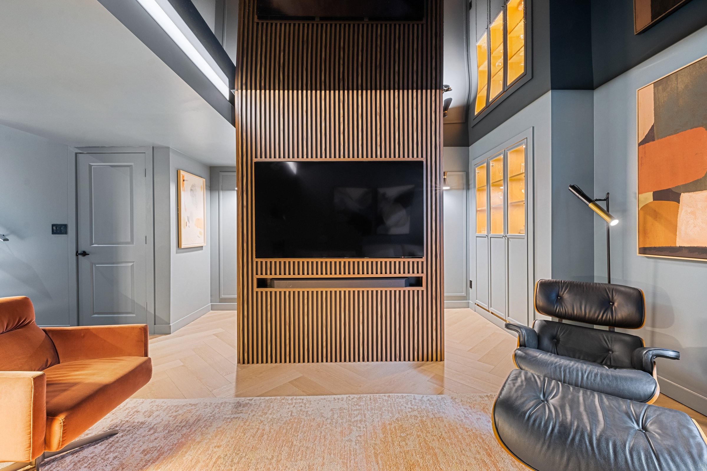 Crestmont basement finished: walnut slatted media wall with television, lit display cabinets and lounge chair