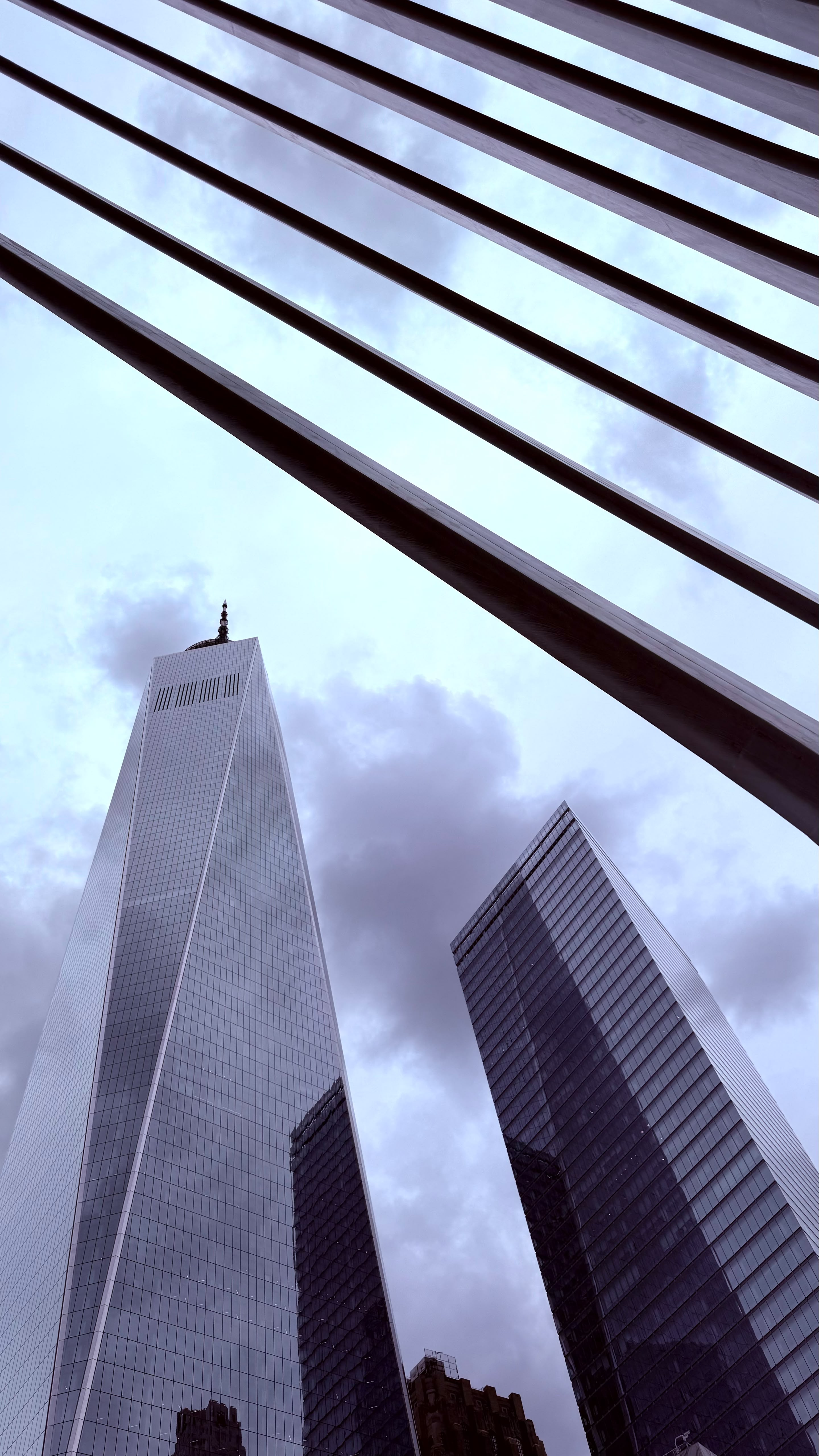 Low-angle view of One World Trade Center and neighboring skyscrapers against a cloudy sky.