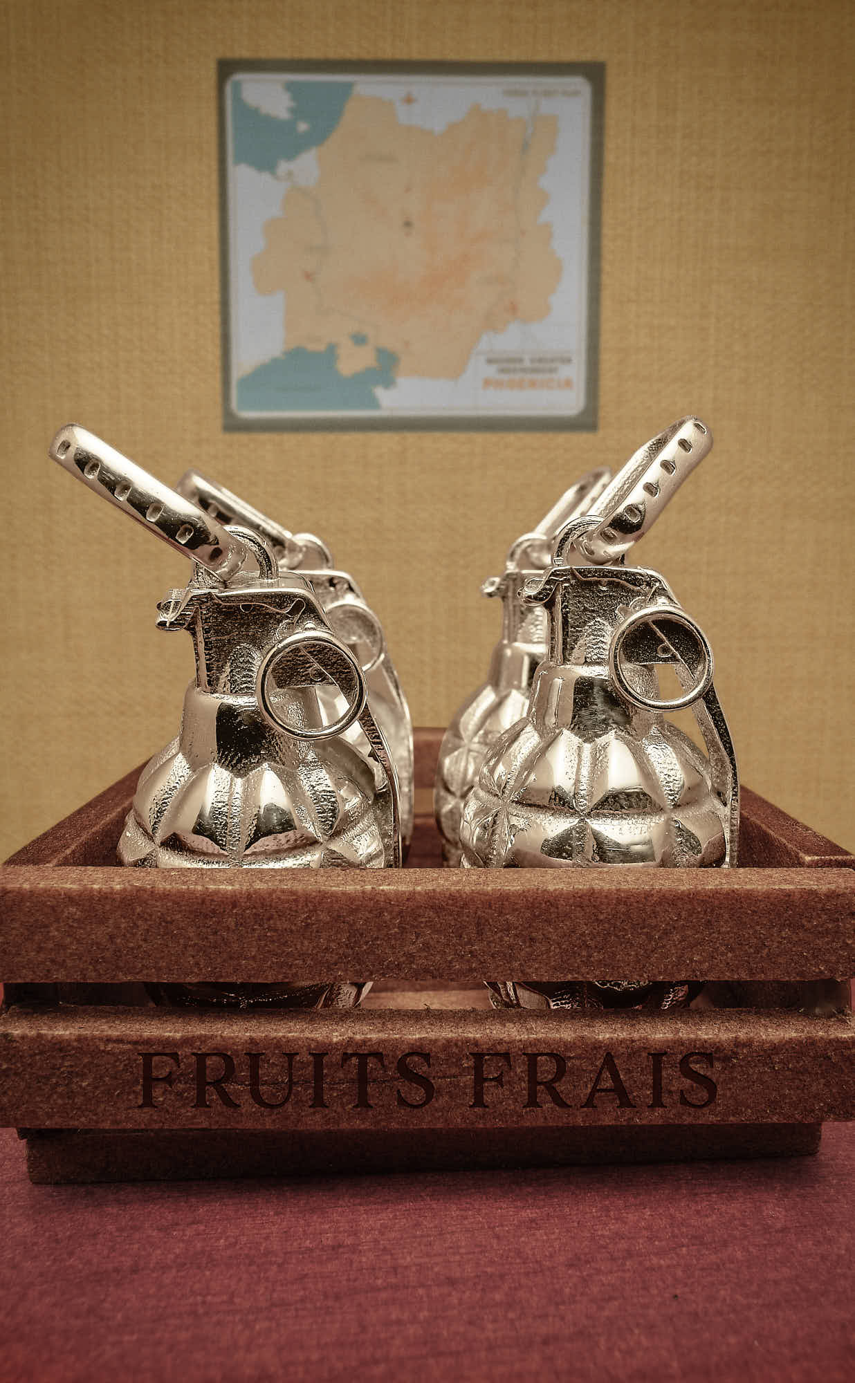 Silver grenades in a wooden crate labeled "Fruits Frais" with a map in the background.