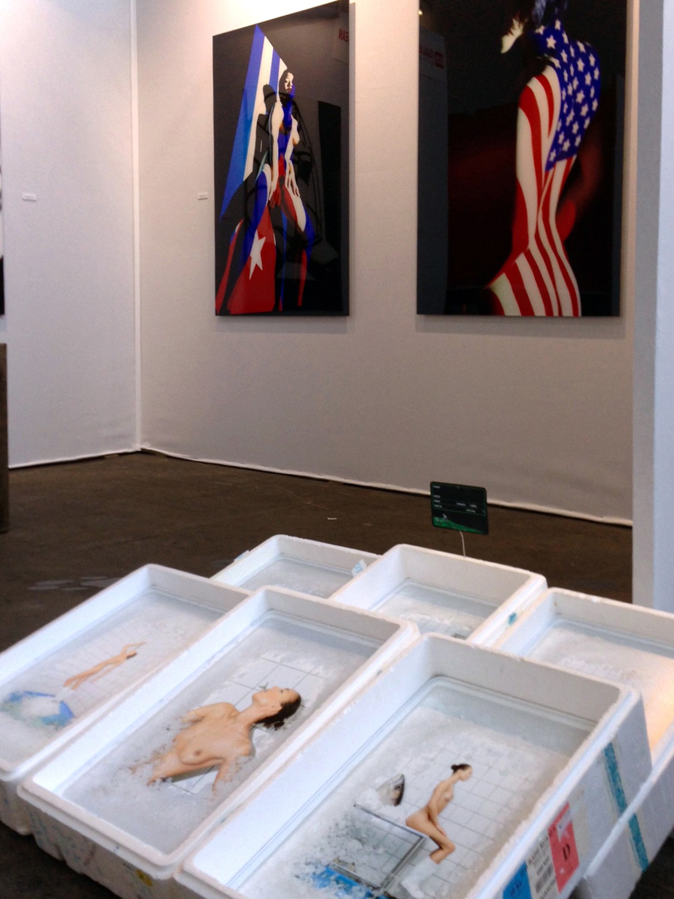 Vue intérieure d’un conteneur d’exposition présentant les portraits en noir et blanc de Frédéric Bourcier, éclairés par des néons au plafond.