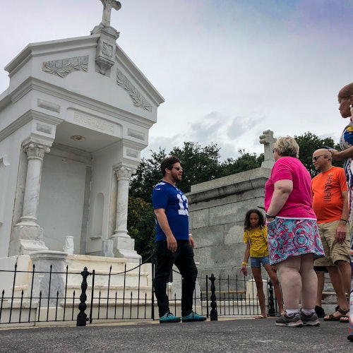 一群人，包括一个孩子，站在公墓中一个华丽的白色陵墓和大理石墓旁边。