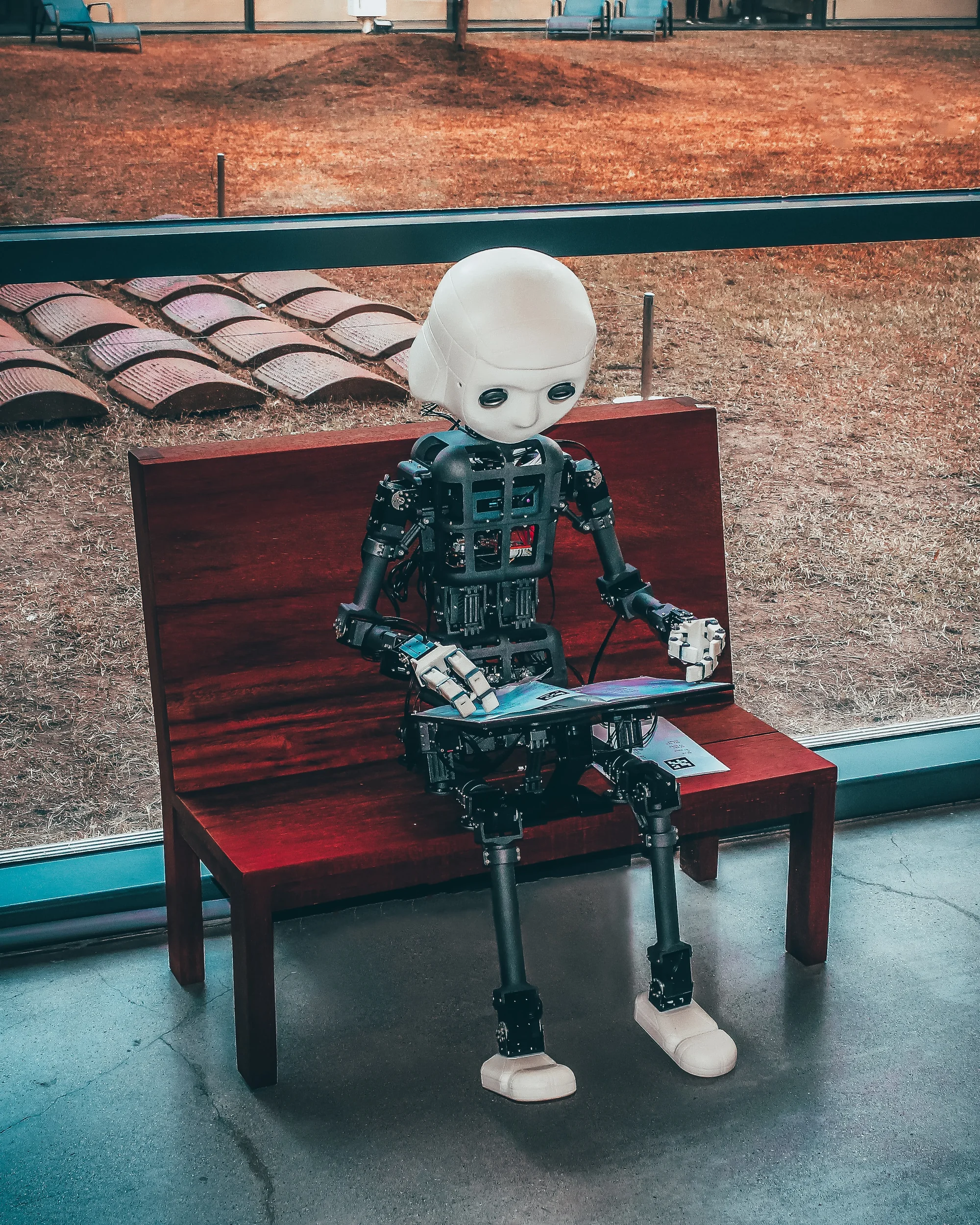 Humanoid robot sitting on bench holding tablet device