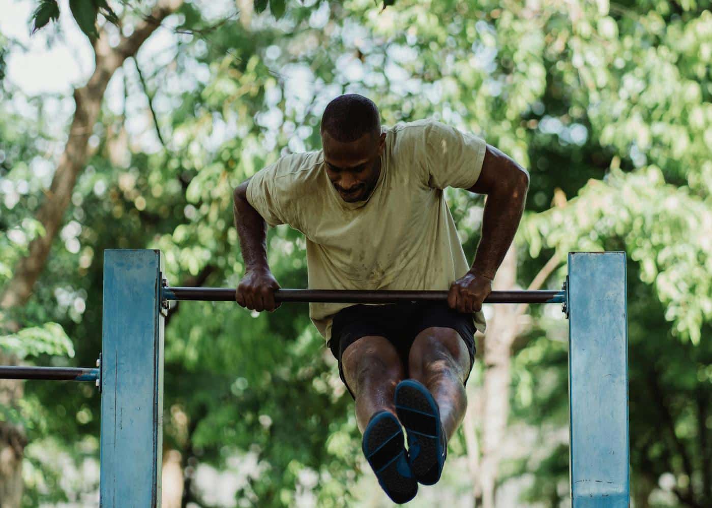 Man lifting himself up on pullup bar with legs stretched out in front of him outdoors