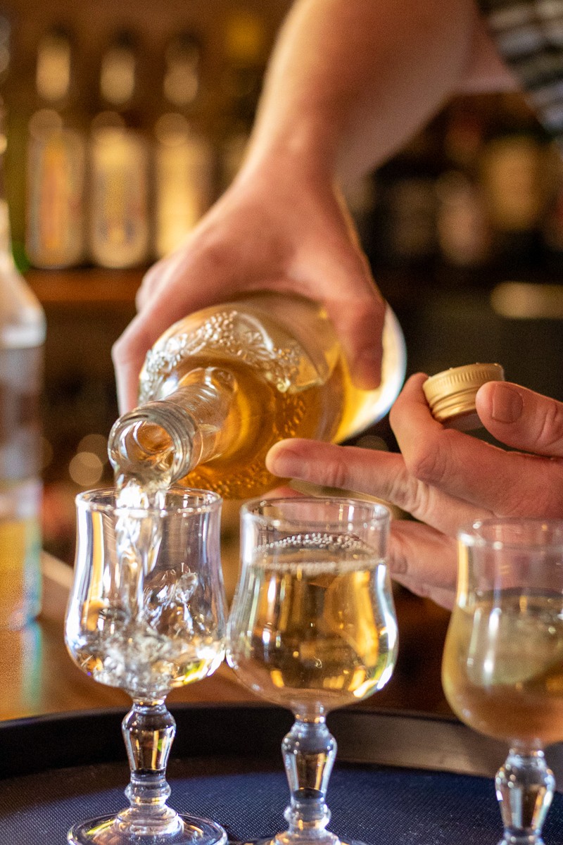 Restaurant interior with wooden tables and chairs lined against a textured wall, softly lit by round wall lamps.