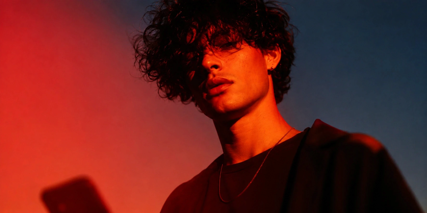 Portrait of a young man with curly hair lit by red and blue light at dusk, shot by photographer Ethan Cole