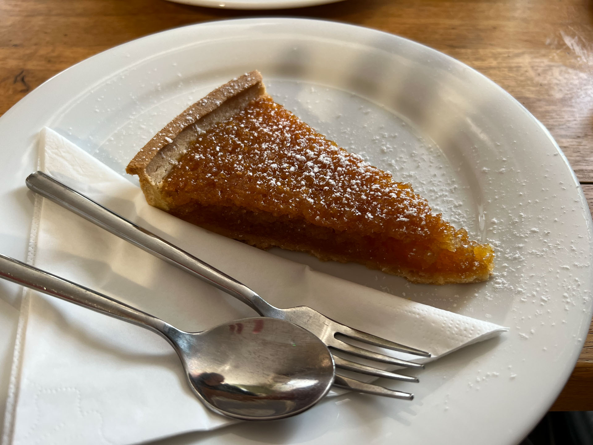 A slice of treacle tart on a plate, with a dusting of icing sugar on.