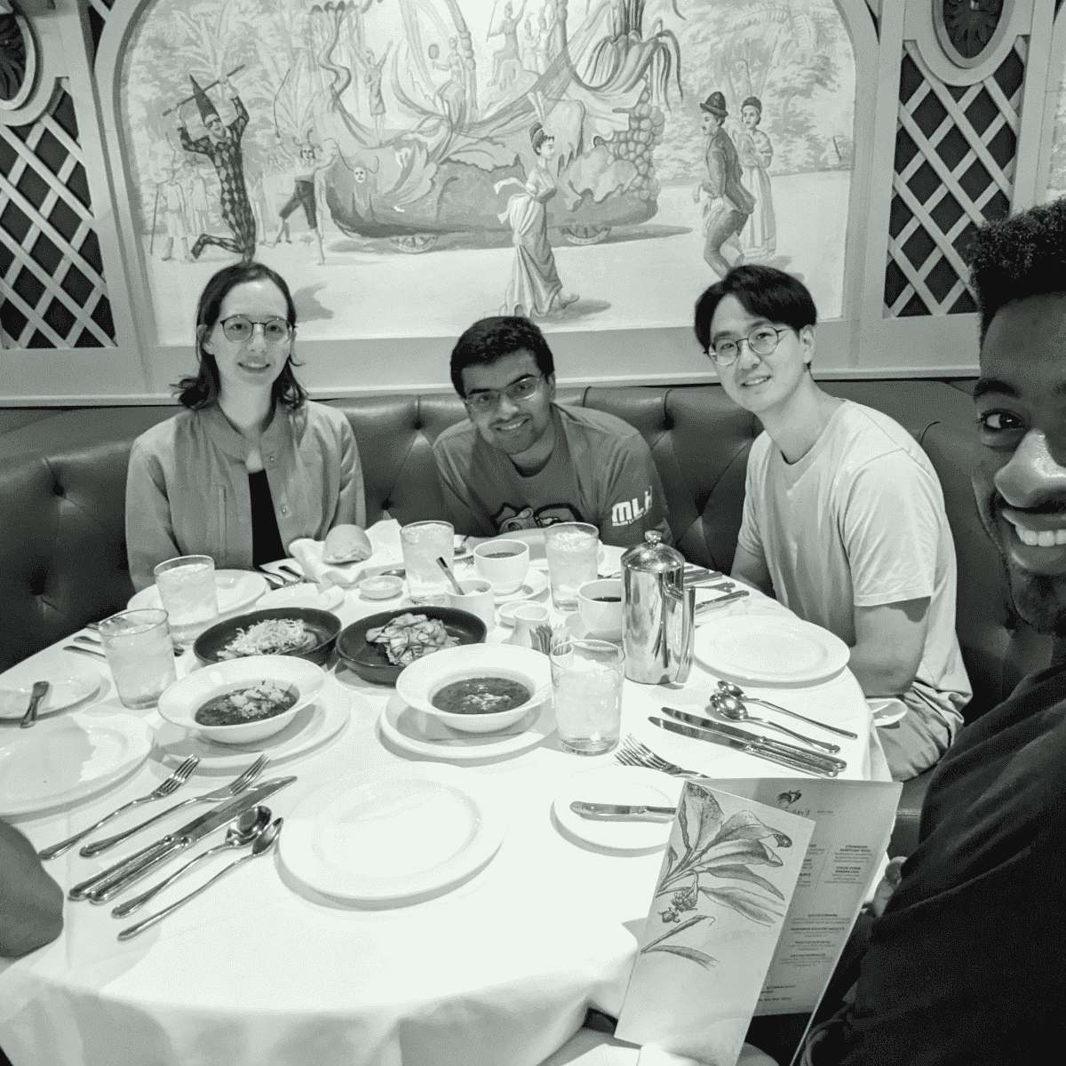 Four friends enjoying a meal at a restaurant with a mural in the background