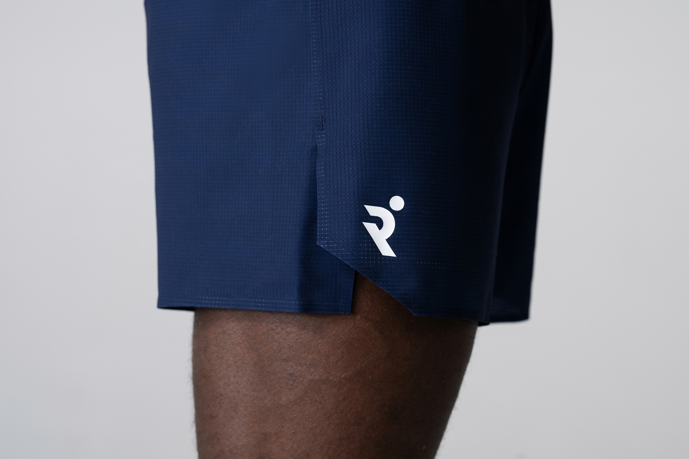 Close-up of navy RUNNA running shorts and white logo.