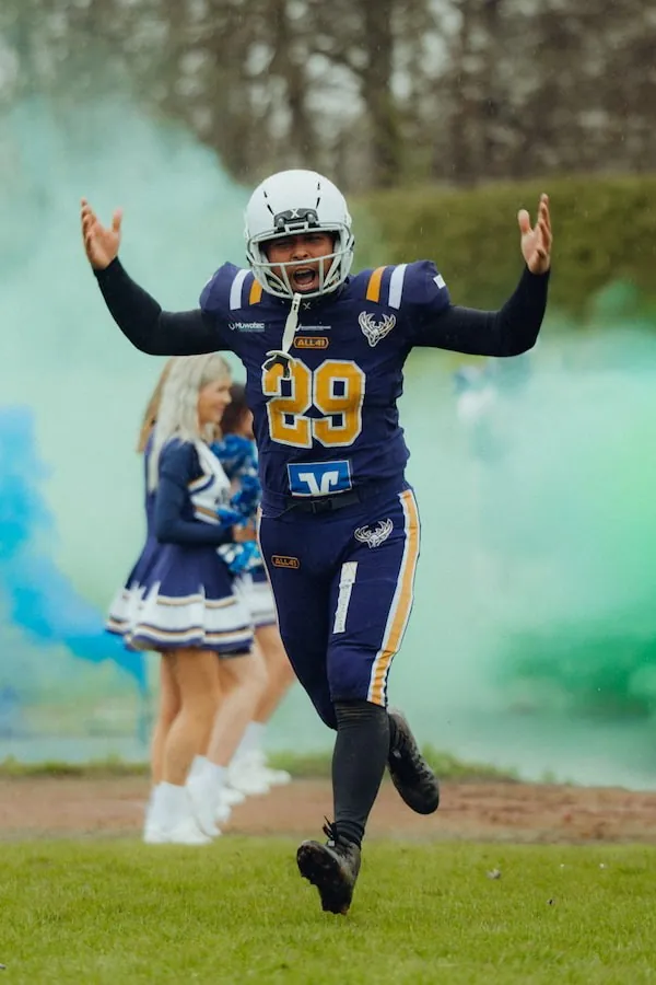 Ein Spieler der Balingen Bucks im blau-goldenen Trikot jubelt mit erhobenen Armen vor blau-grünem Rauch, dahinter Cheerleader.