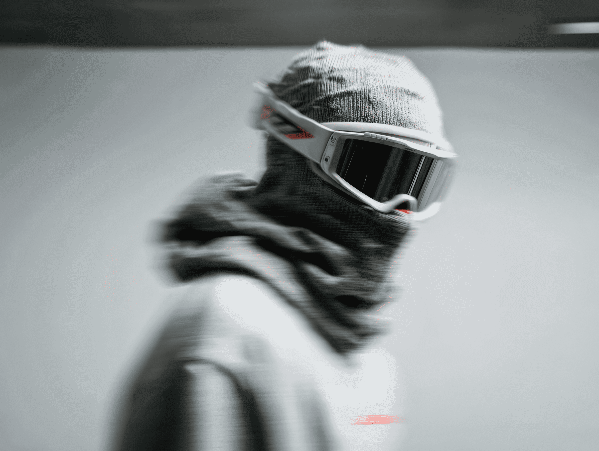 Person wearing white ski goggles and a knitted hood, facing sideways with motion blur.