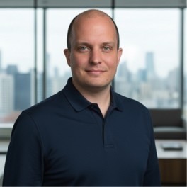 Smiling young woman with long hair standing against a dark green background, holding a finger to her chin.