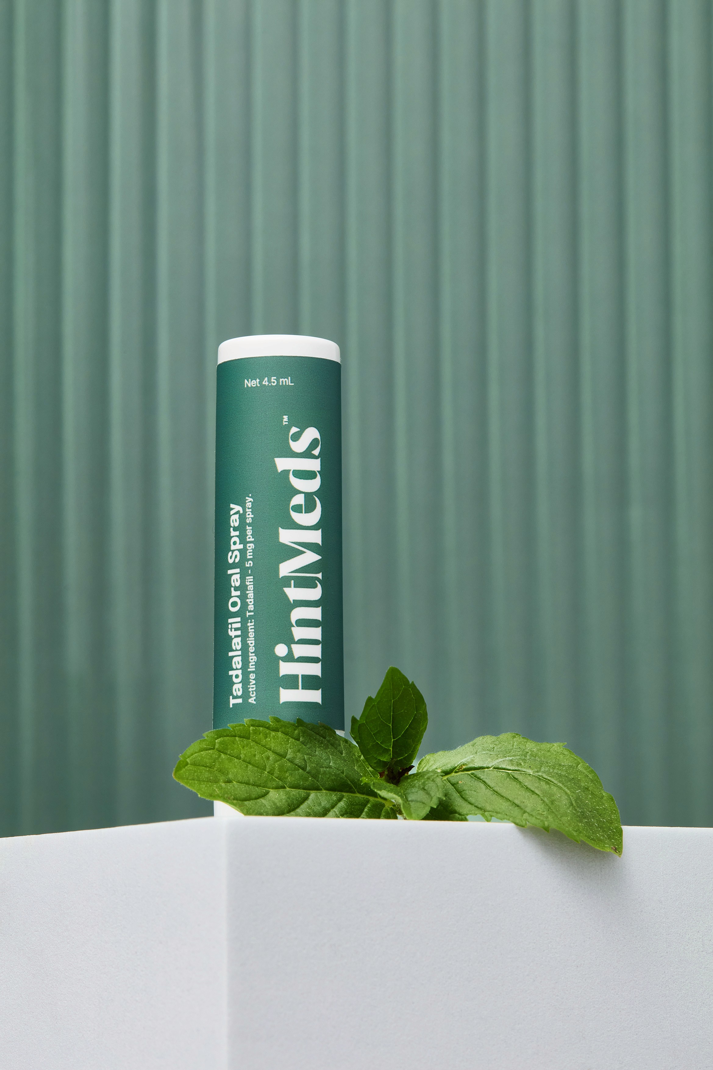 A green beverage can placed on a white surface, surrounded by fresh leaves, against a textured green background.