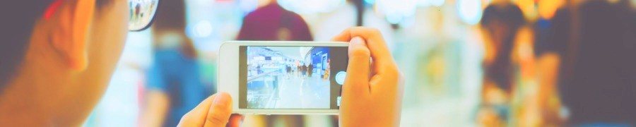 Hands holding a smartphone photographing a storefront in a shopping area