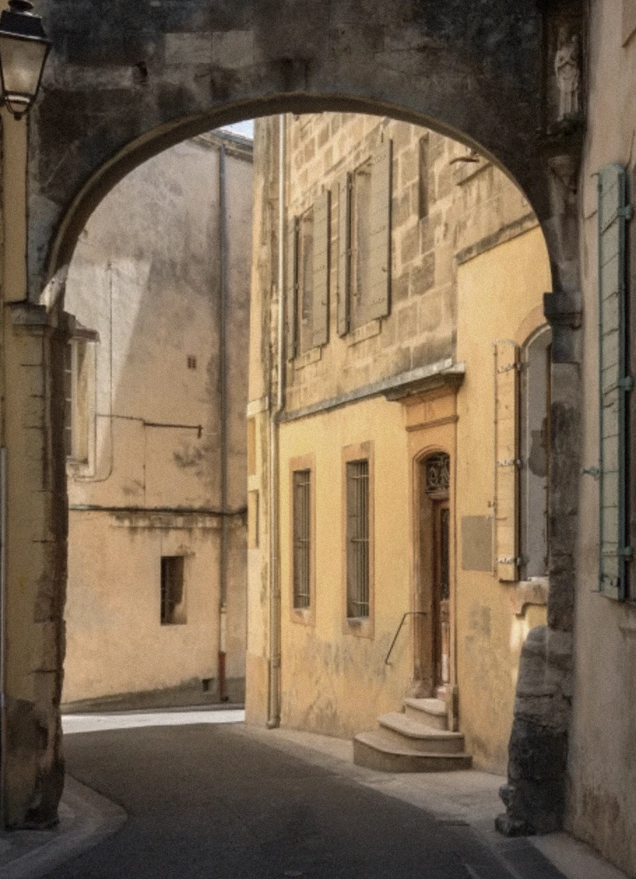 Sunlit stone alleyway framed by an old arch in a quiet southern French village.
