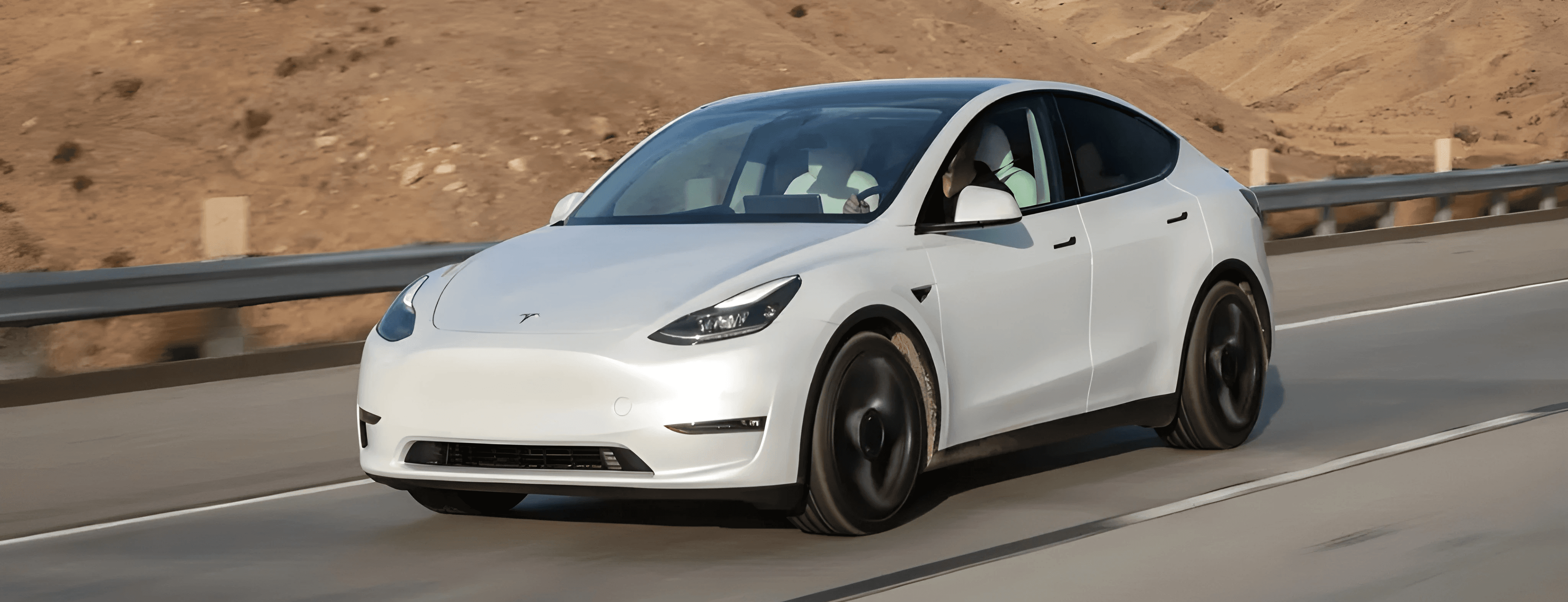 Tesla Model Y blanche sur route ouverte, SUV électrique vu de face dans un décor désertique et montagneux