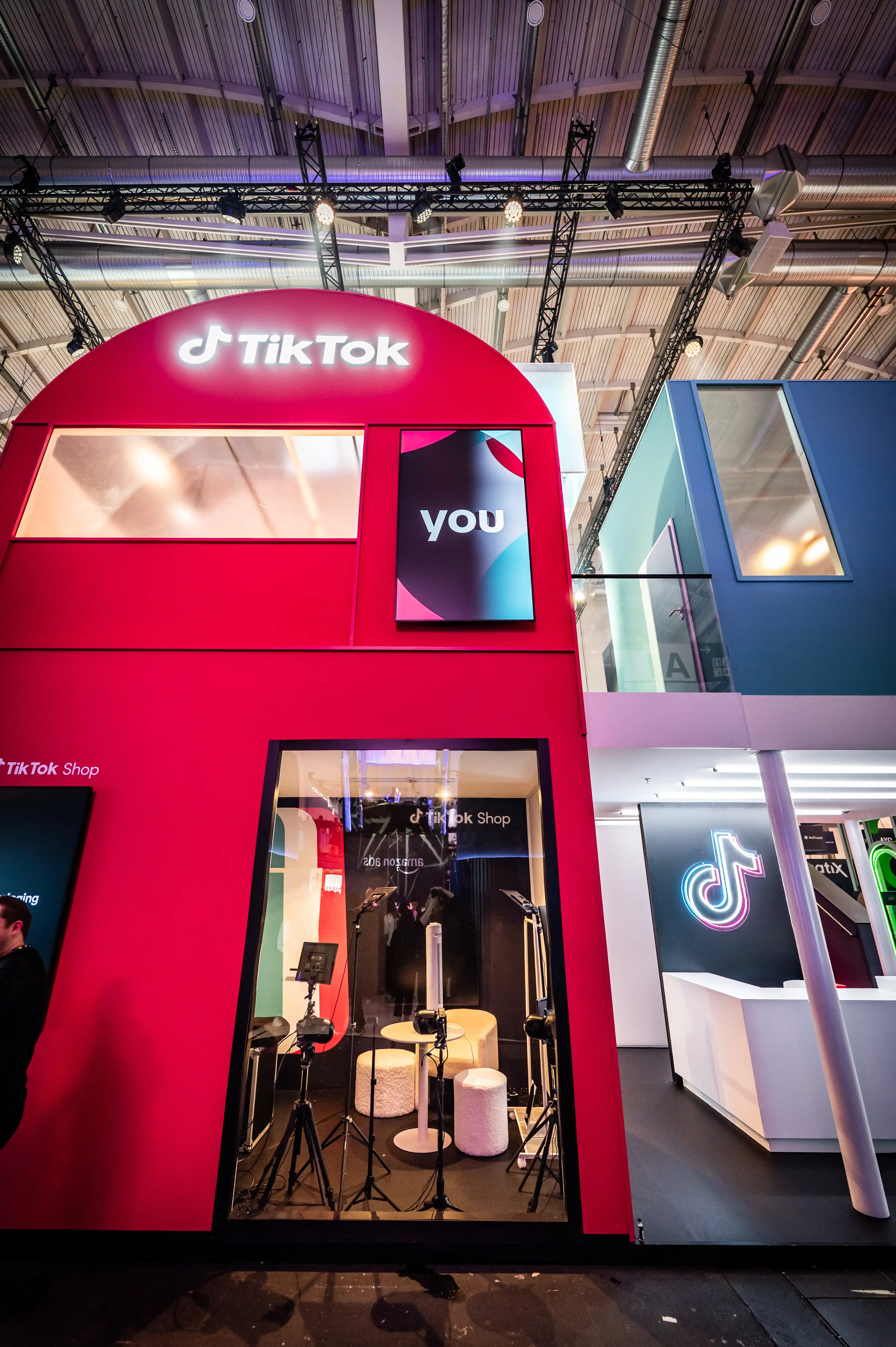 Red arched booth facade with TikTok sign and view into the TikTok Shop studio with stools and microphones.