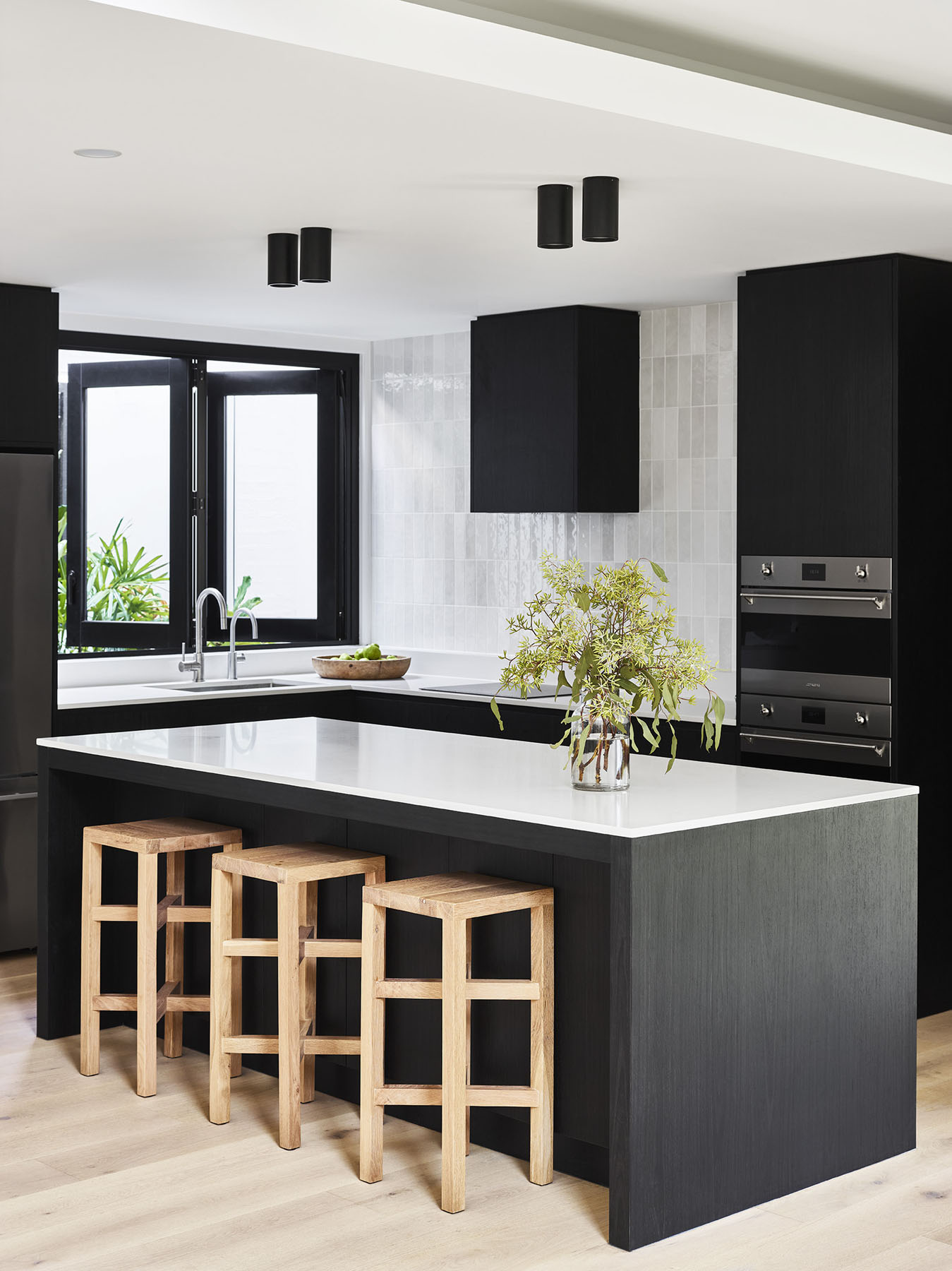 Modern kitchen with black cabinetry, white island bench, and timber stools.