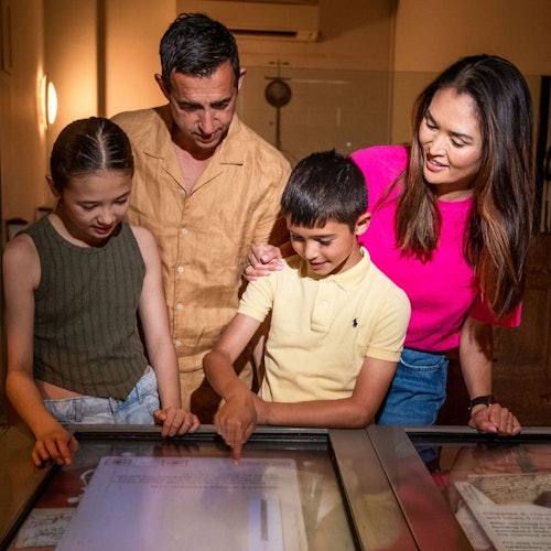 شخصان بالغان وطفلان ينظرون إلى طاولة عرض في متحف أو قاعة معارض.