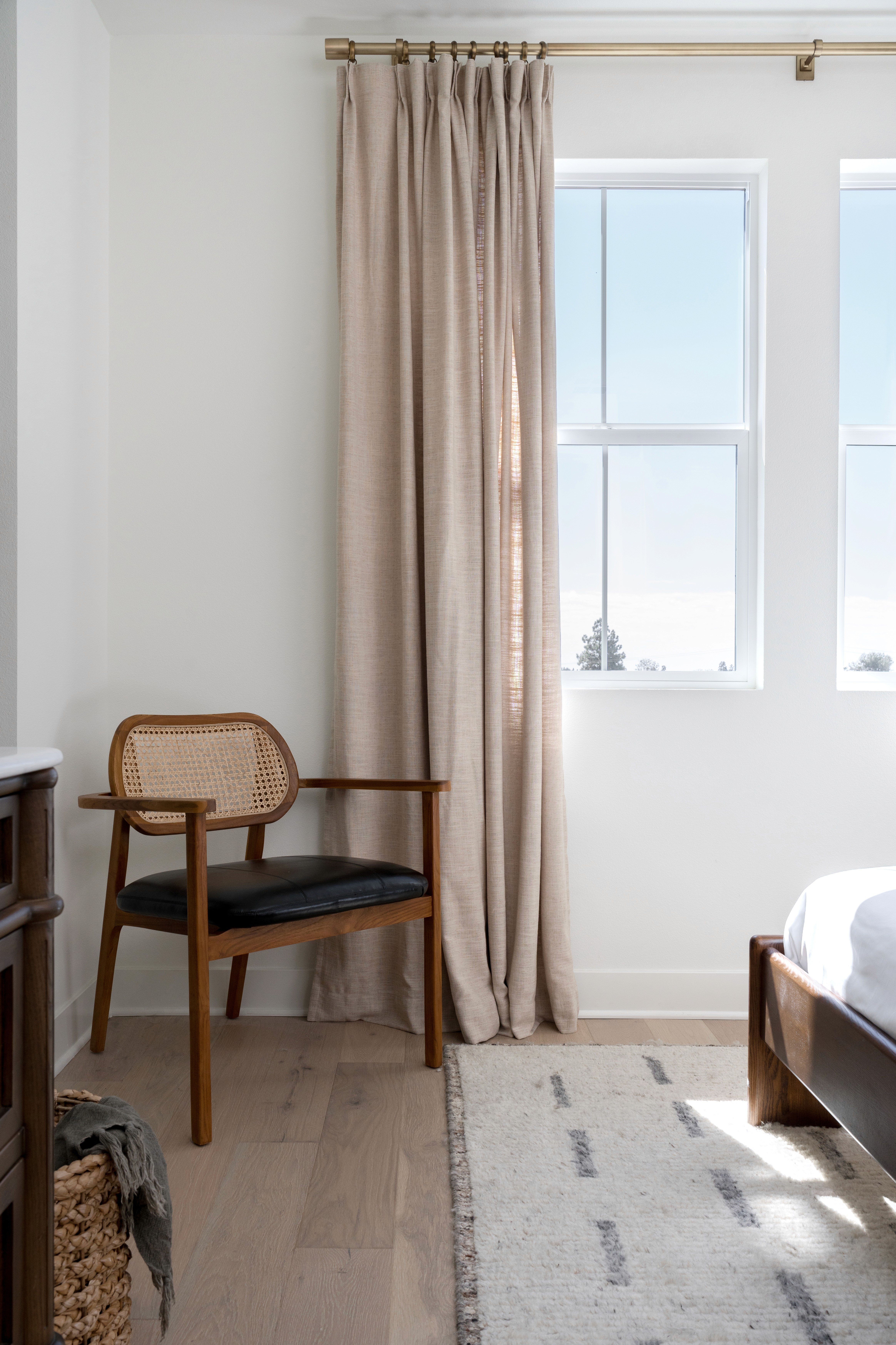 View of foot of bed towards windows with beige curtains to the floor and mid-century modern accent chair