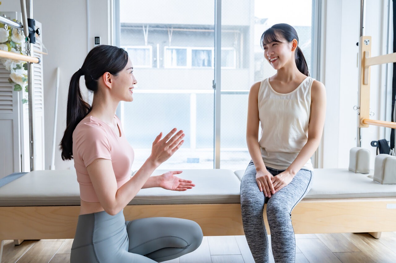 明るい室内で向かい合って話す二人の女性。個人の健康情報を持ったAIが、医療機関での治療以外の選択肢も含めて健康相談に応じる場面を表す