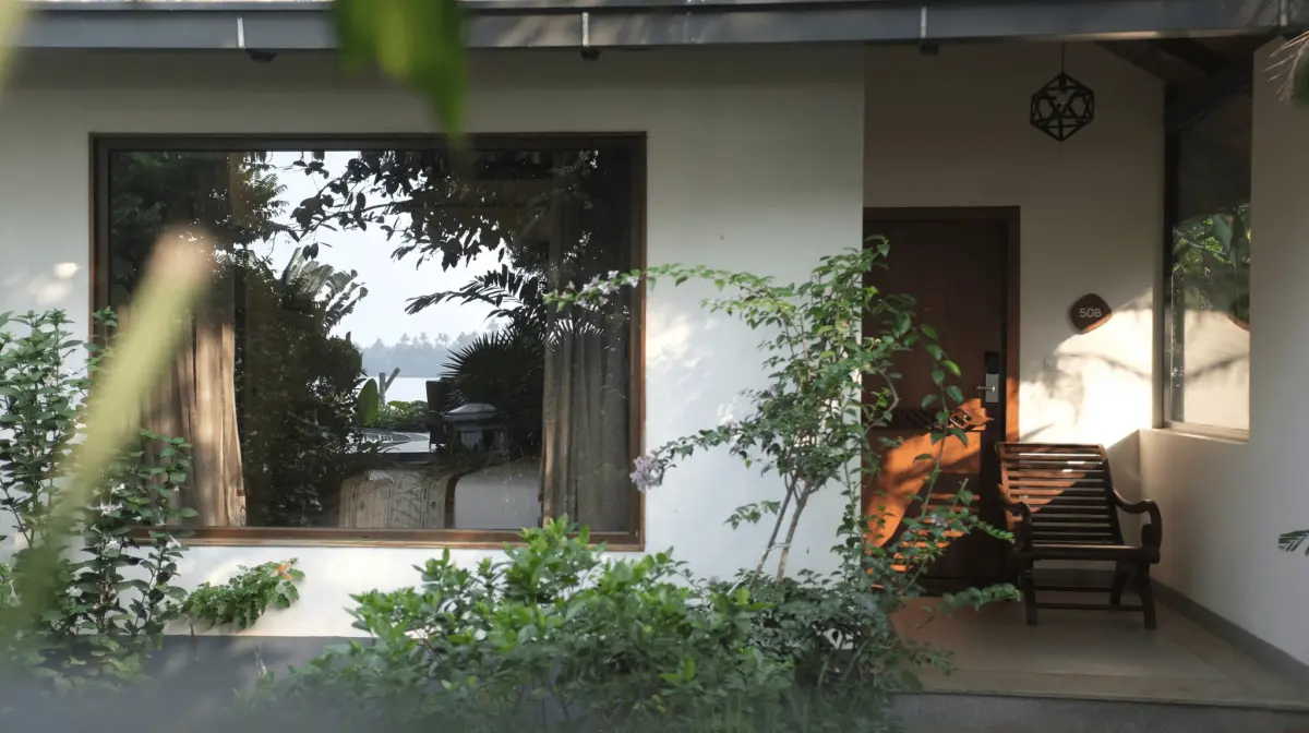 Junior Suite entrance at Vedic Village Kodungallur with a wooden bench, private door and large window reflecting the garden and lake