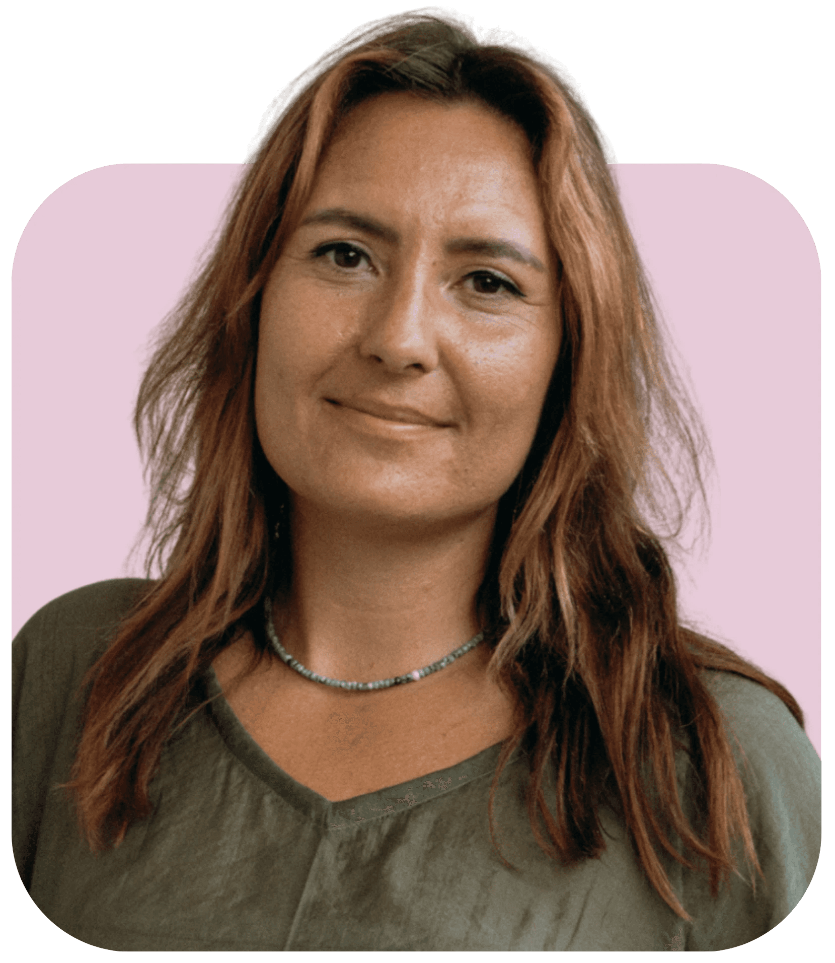 A woman with long brown hair smiles, wearing a green shirt, against a soft pink background.