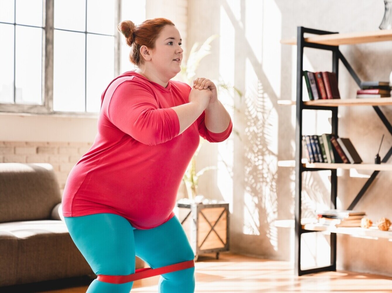 overweight woman doing fast weight loss exercises by using a resistance band to do squats