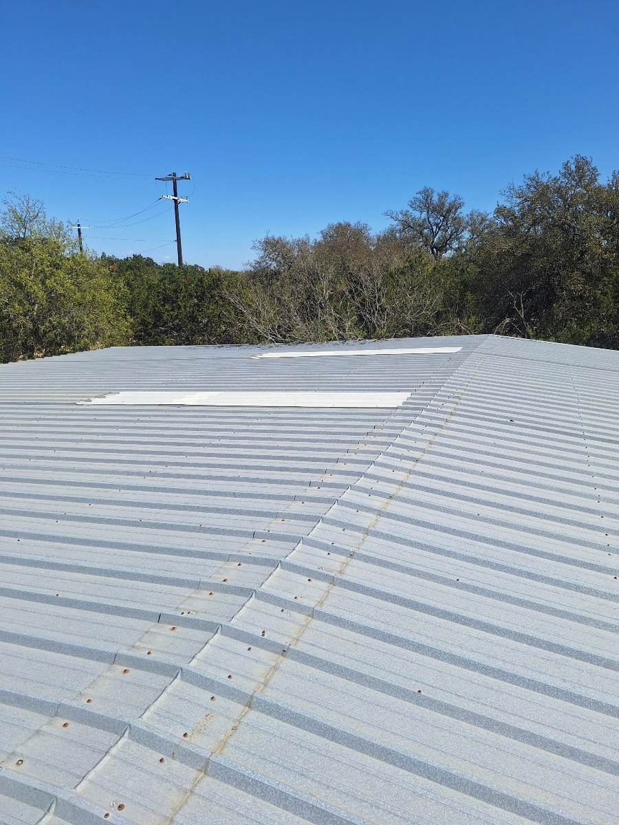 Actual exposed-fastener metal roof with visible screw rows, ribbed panels and ridge cap.