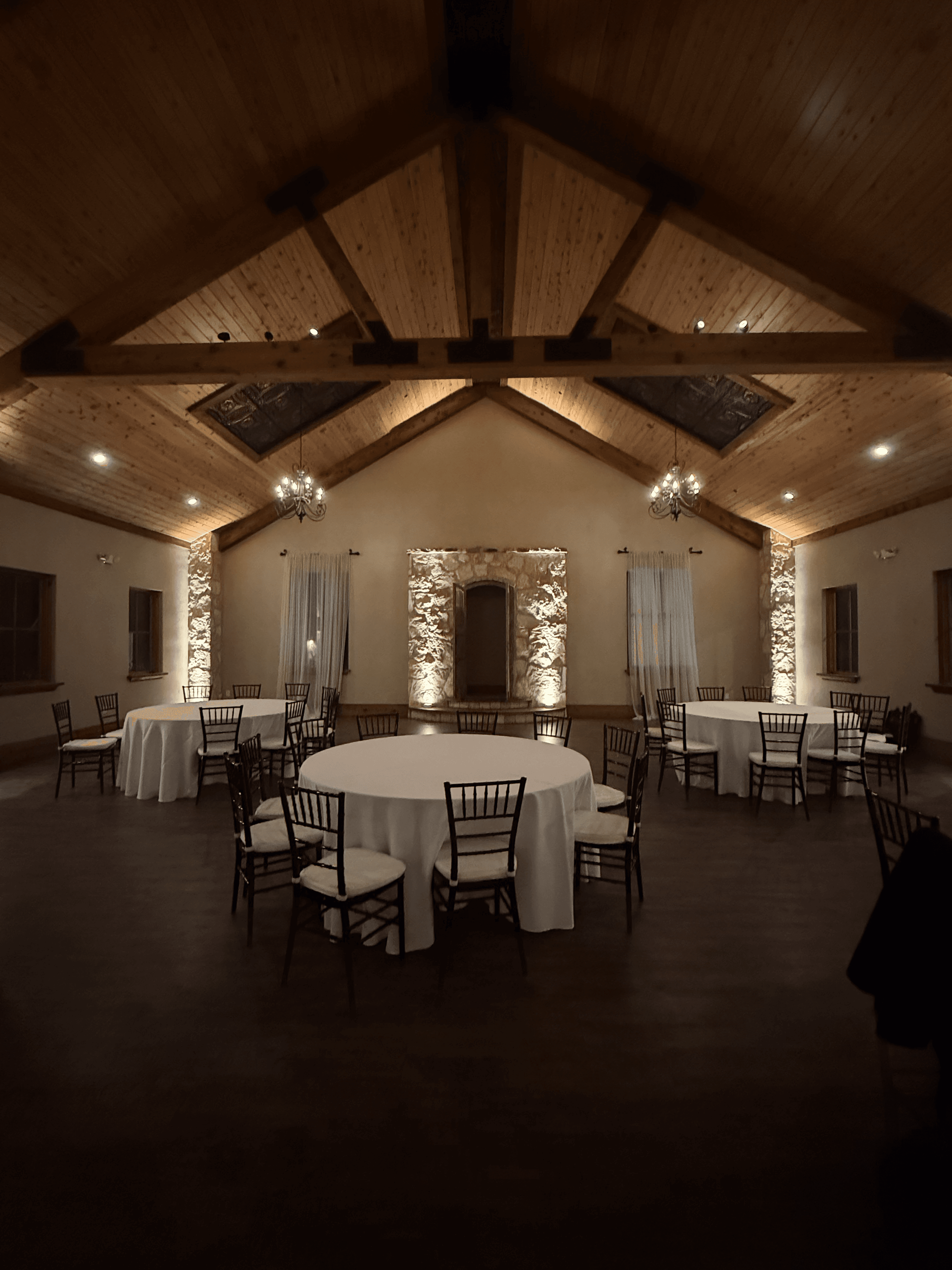 Elegant event venue with round tables set for a celebration, illuminated by warm amber uplights to create a sophisticated atmosphere