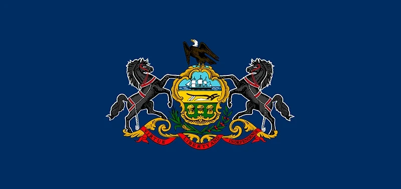 The Pennsylvania state flag features a dark blue field with the state coat of arms in the center. The coat of arms includes two black horses flanking a shield, an eagle perched atop, and a red banner below.