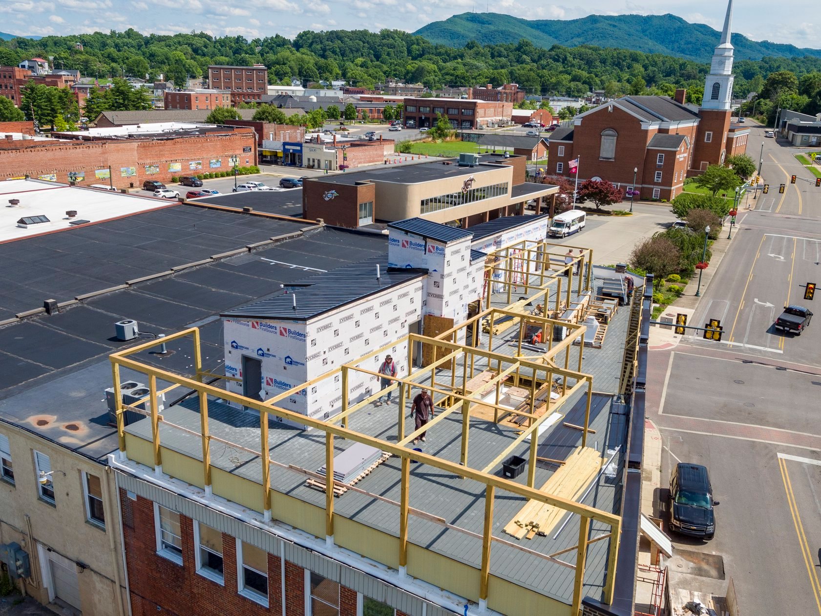 Aerial view of urban buildings with rooftops, showing details like vents and greenery in a city setting.