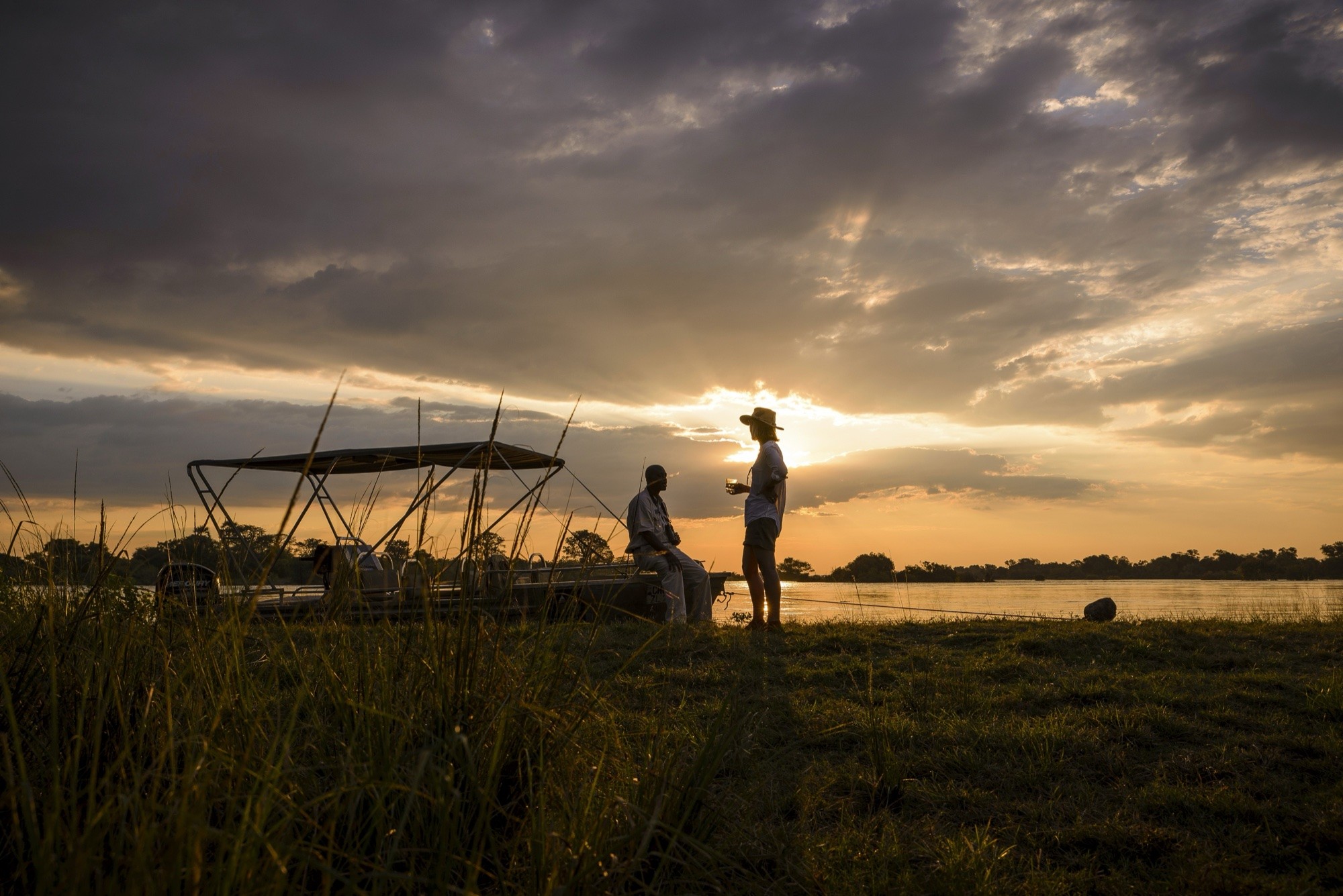 Guests sharing sundowners by the boat at a river's edge