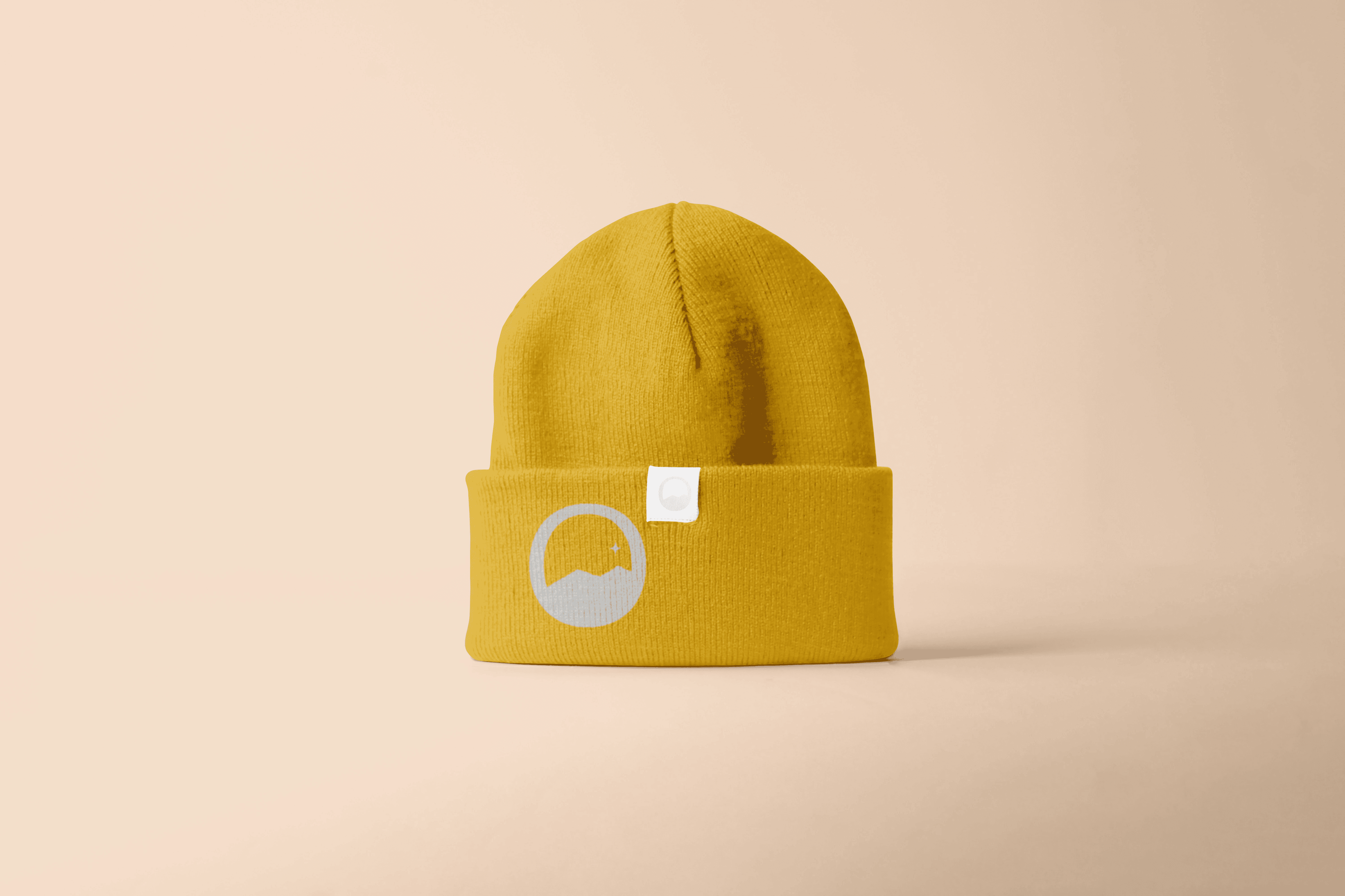 Photo of a mustard yellow beanie with a logo on the front with a peach background