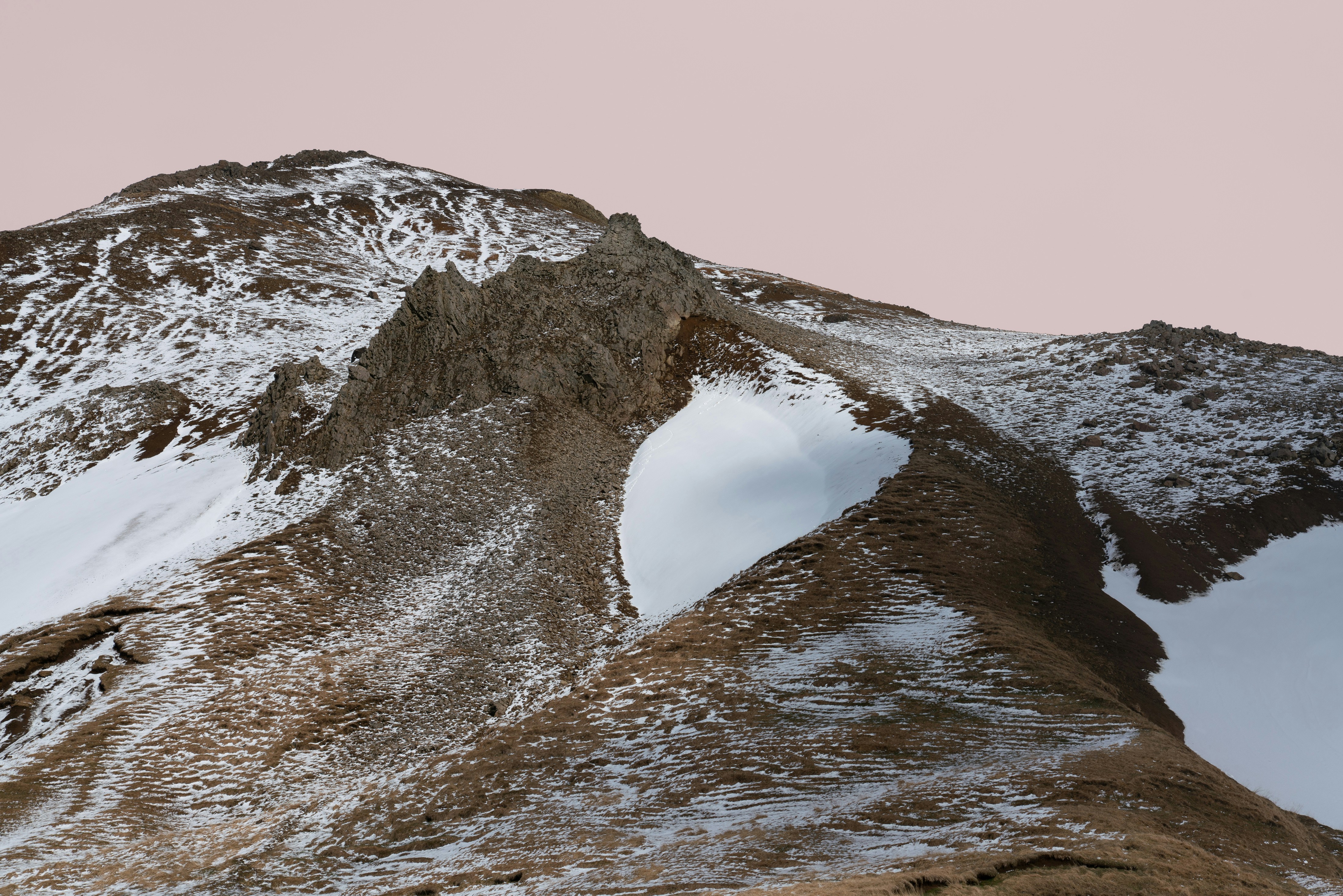 Snow-covered mountain peak under a pale pink sky