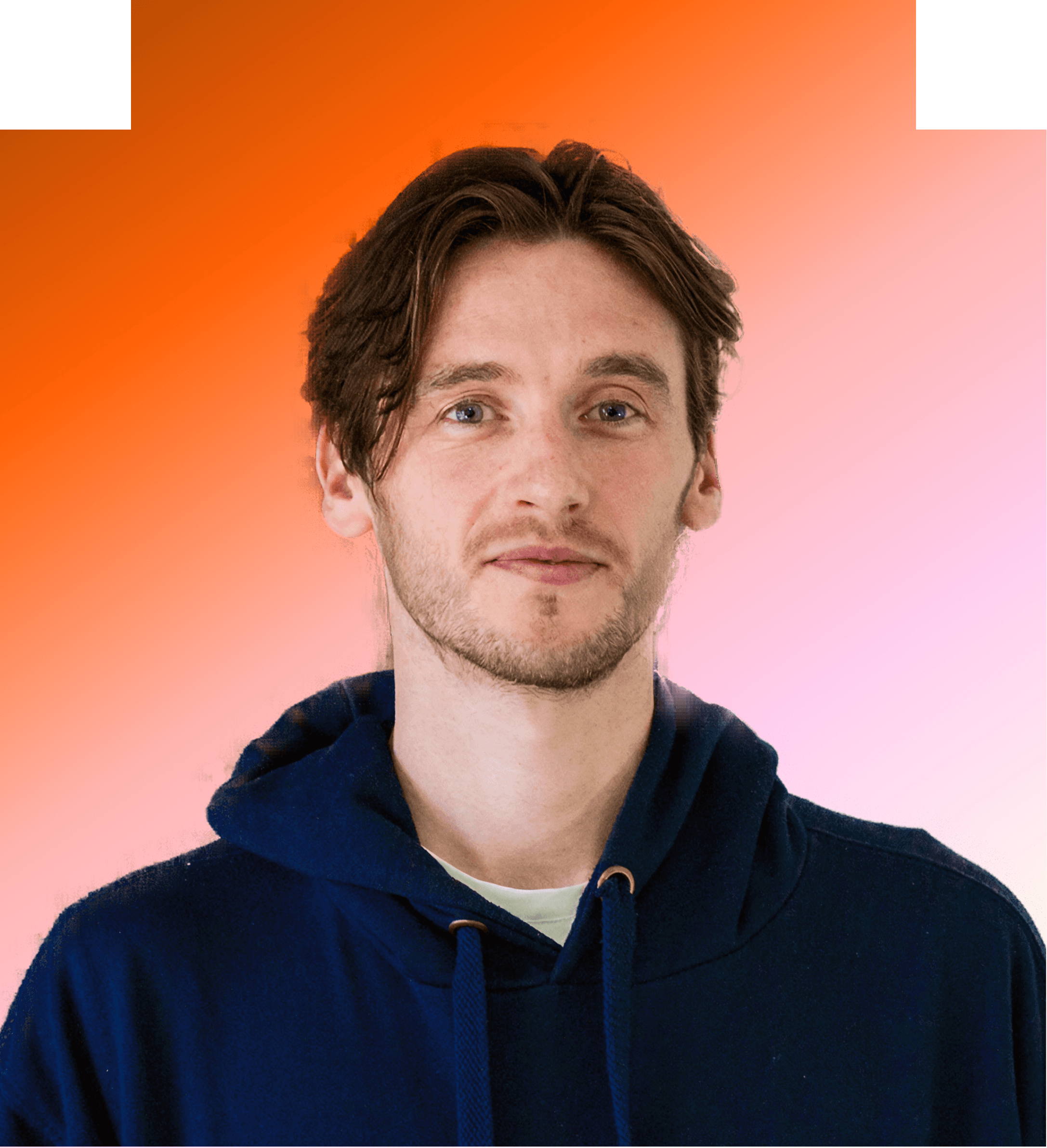 A person with a colorful shirt and blue sweater posing in front of an orange background.