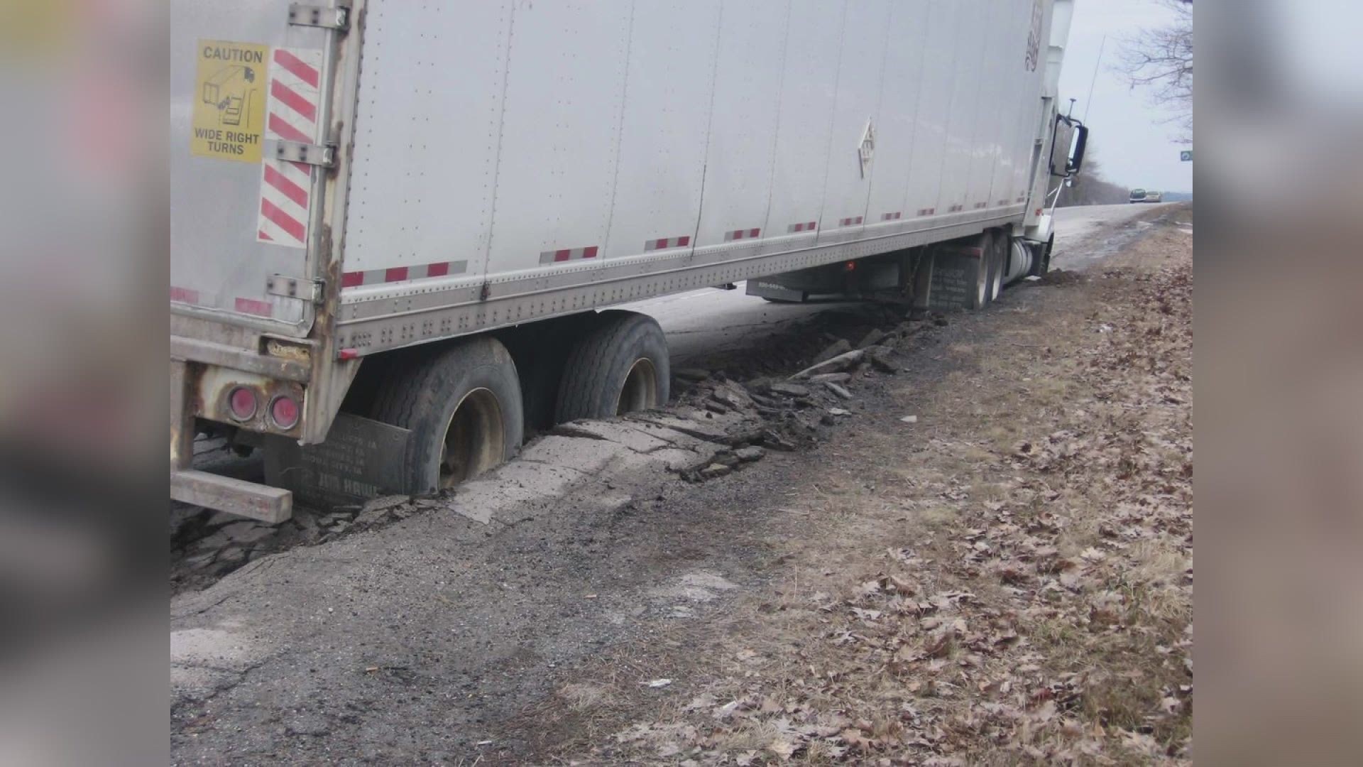 A damaged regional Western Australia road with a heavy freight truck maneuvering around potholes and uneven surfaces.  