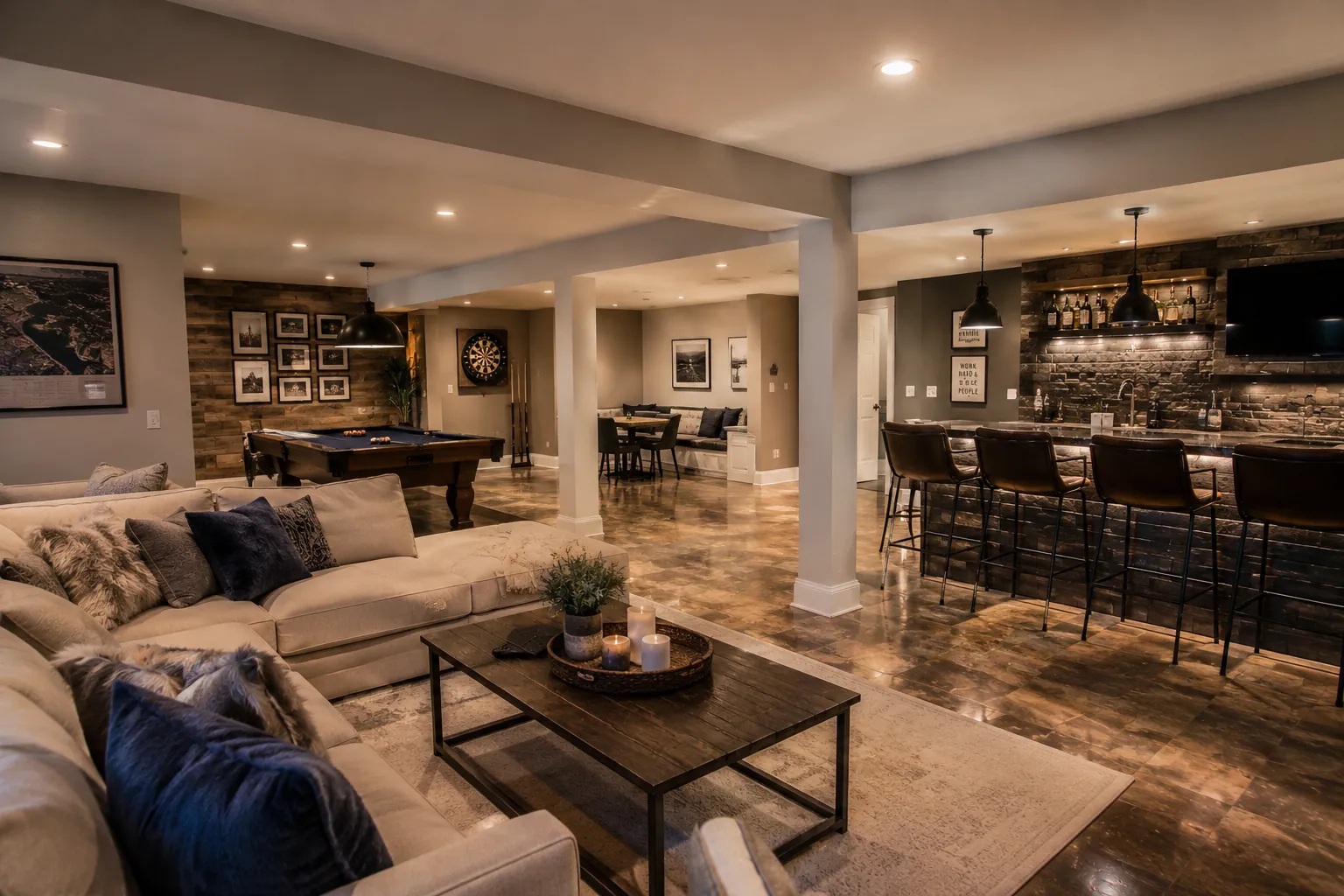 Spacious entertainment basement featuring pool table, full bar with stone accent wall, cream lounge seating, and polished concrete flooring throughout open layout.