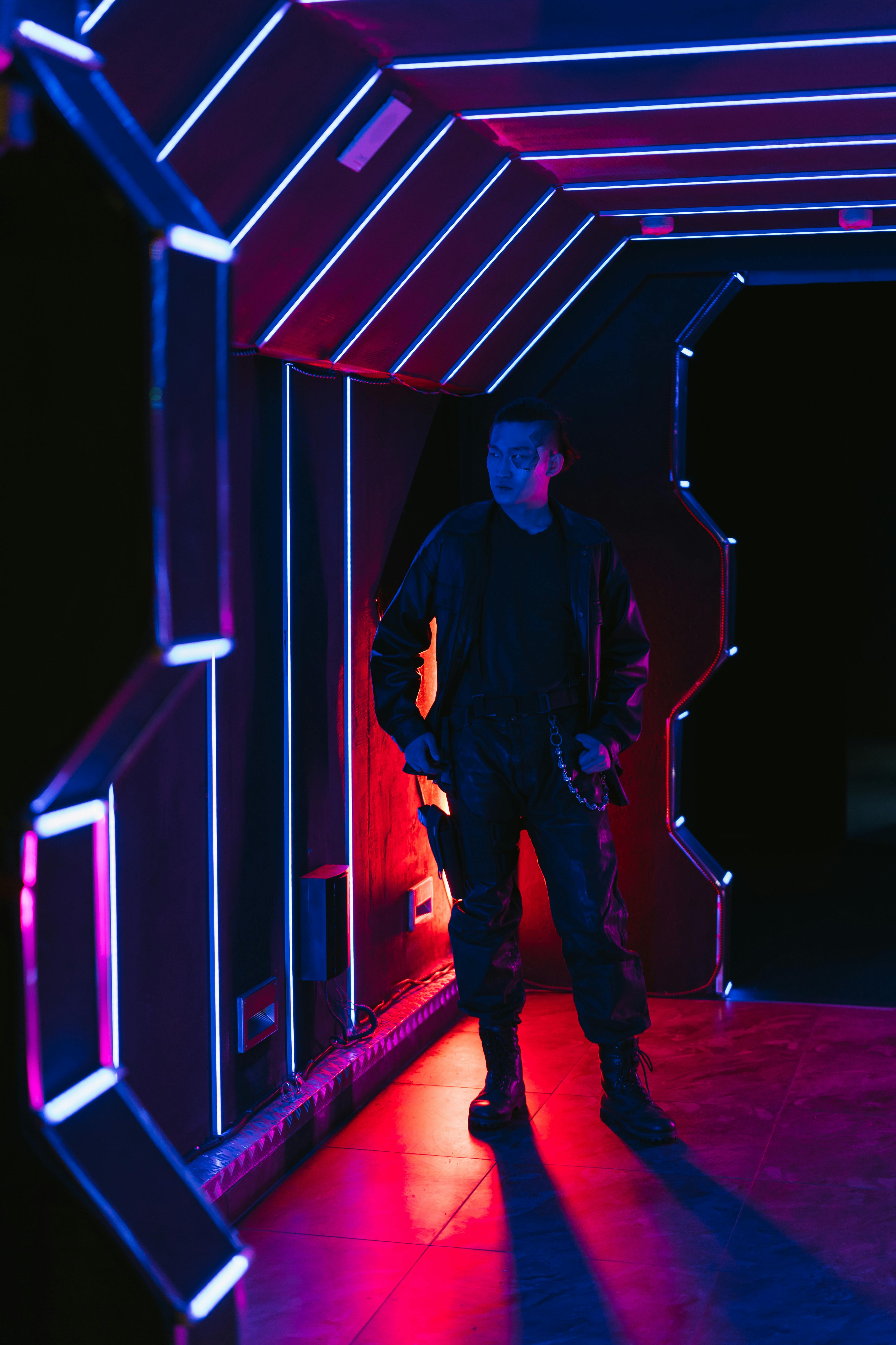 A young person with curly hair smiles at the camera while sitting in front of a laptop against a dark background.