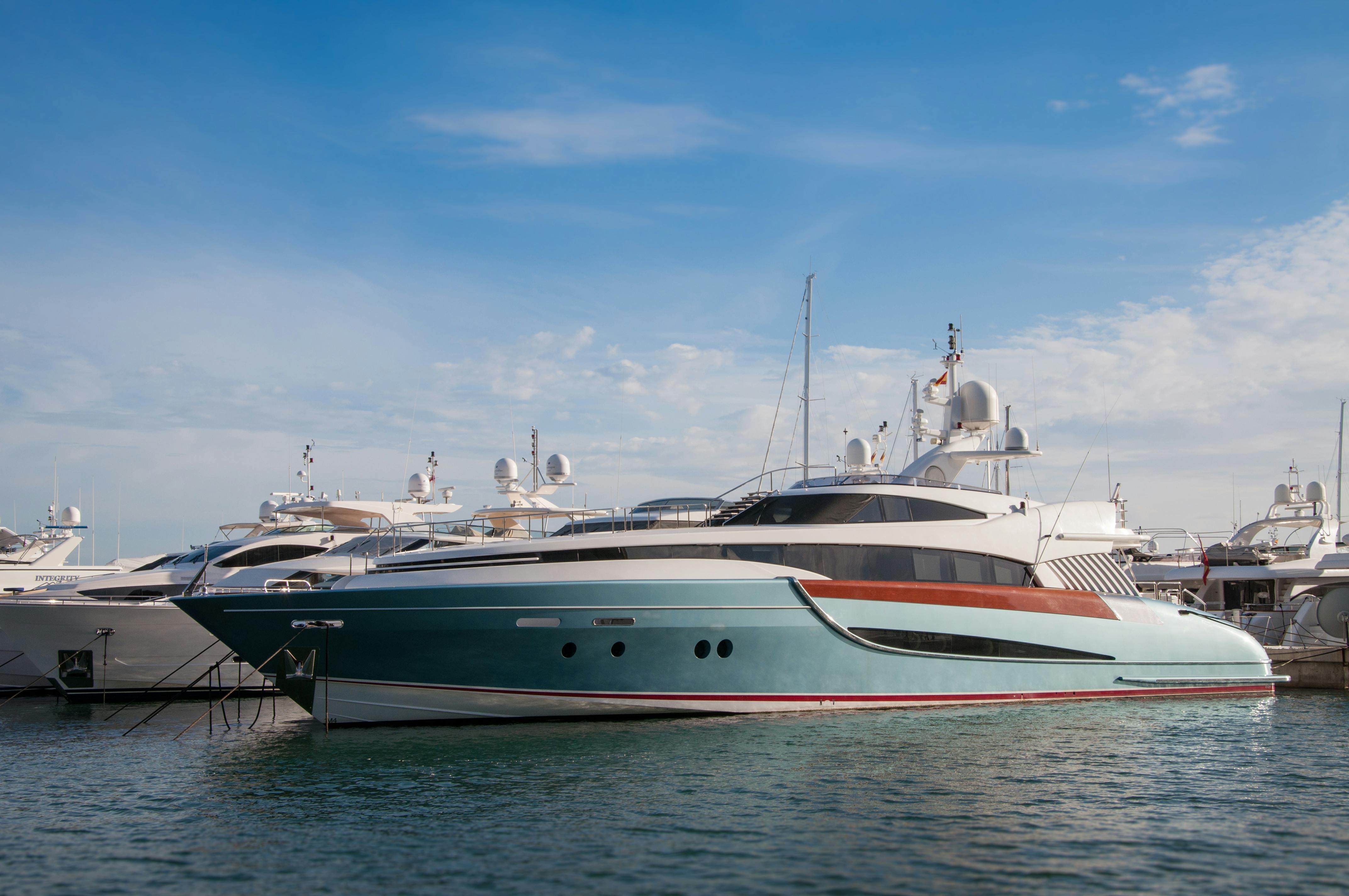 A luxurious turquoise and white yacht with sleek lines is moored in a marina, surrounded by several other vessels under a clear blue sky.