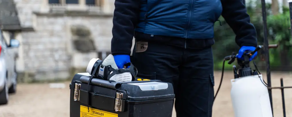 Professional pest control technician in uniform with treatment equipment and spray tank preparing for restaurant in London