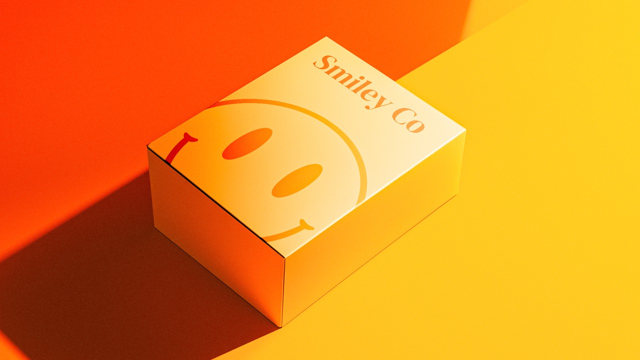 Rectangular packaging box with a pale yellow-to-orange gradient, featuring a large half-smiley face and “Smiley Co” branding, set on a split orange and yellow background.