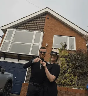 Person standing in the doorway of a brick house holding what appears to be keys