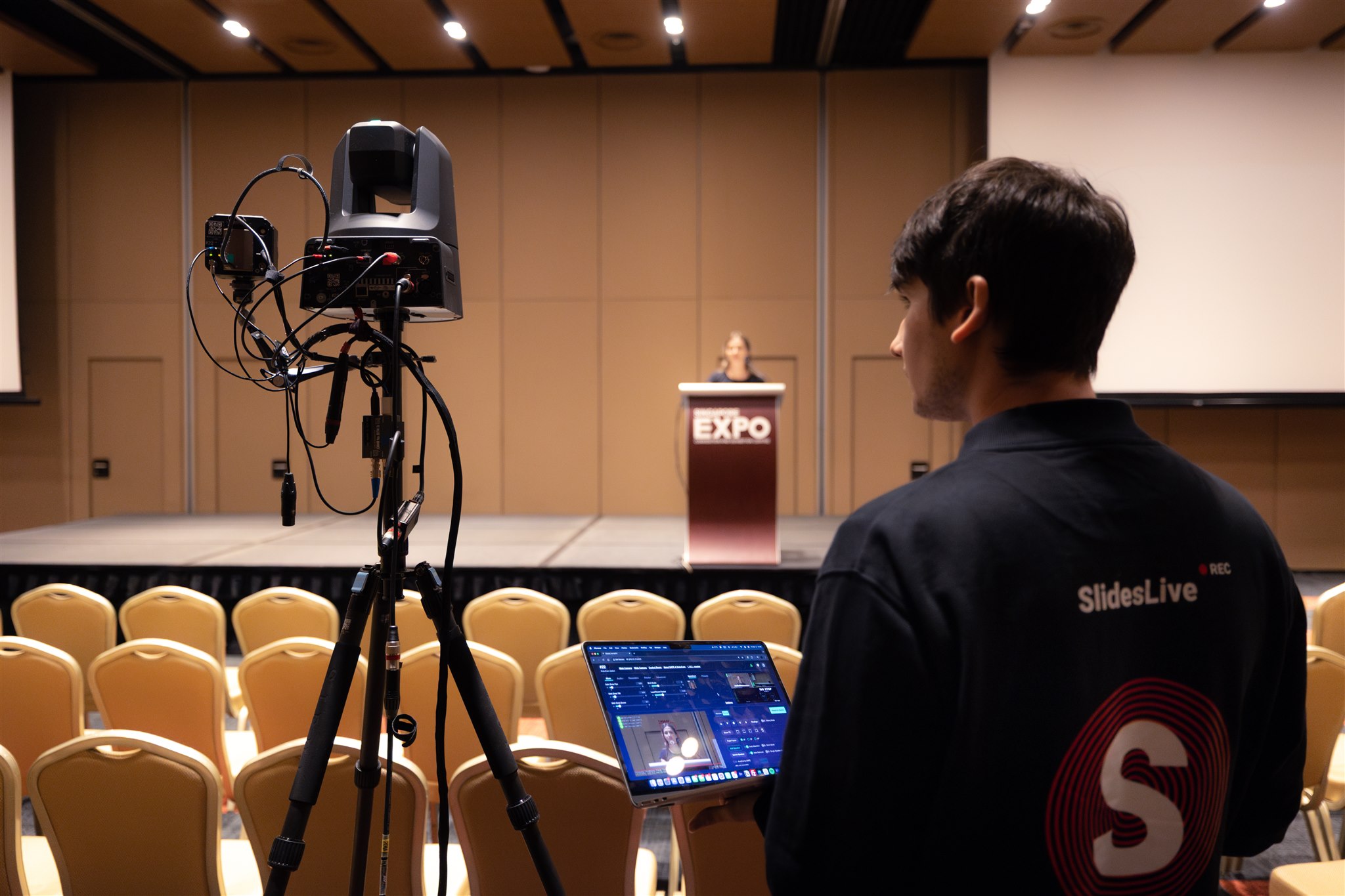 Robotic camera tracking a speaker, with the SlidesLive team visible in the background.