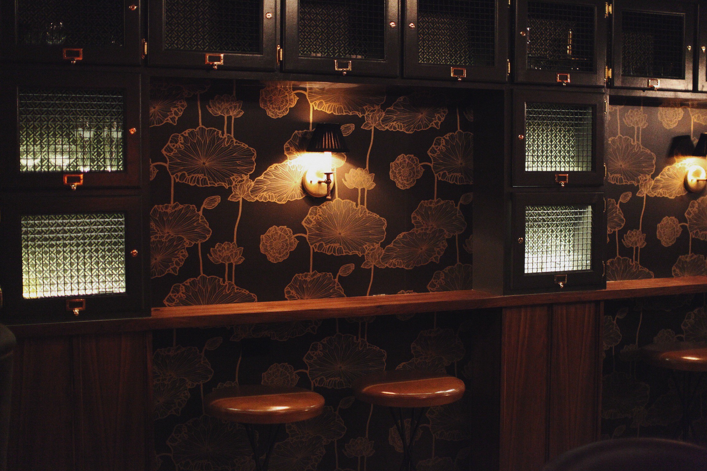 The Walker Inn bar: lotus wallpaper, grille-front cabinets, brass sconces and stools at the counter